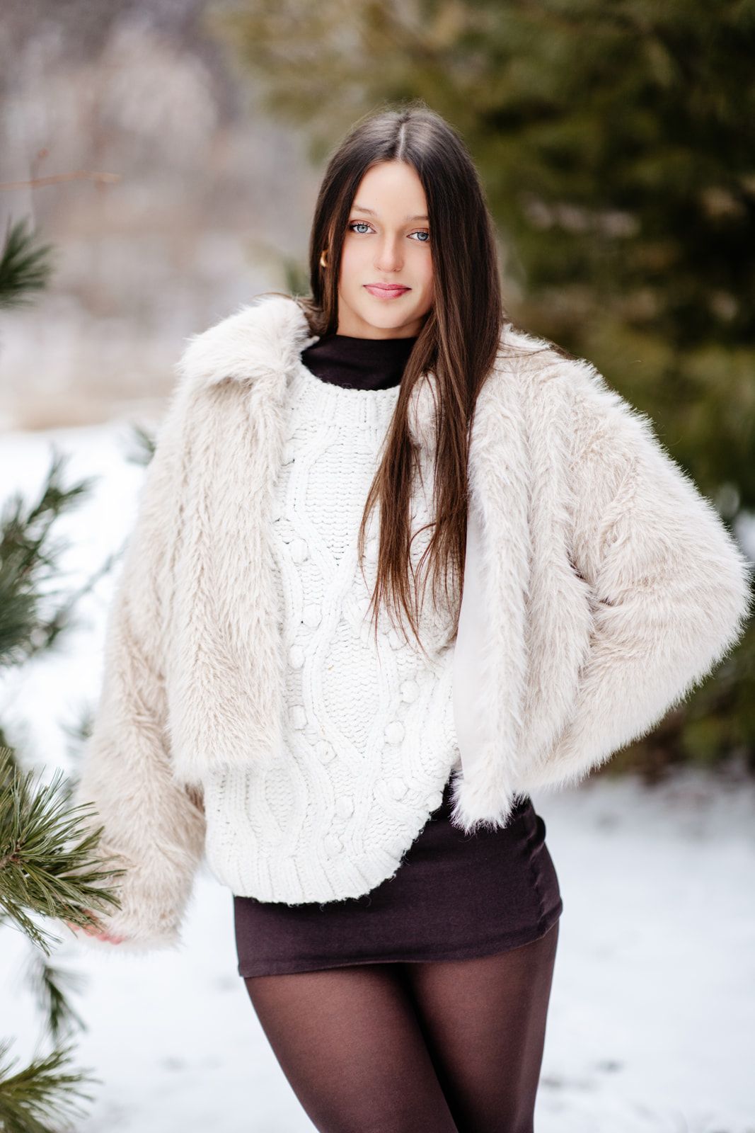 Beautiful brunette woman with blue eyes wearing white faux fur jacket and black turtleneck sweater outdoors in winter snow.