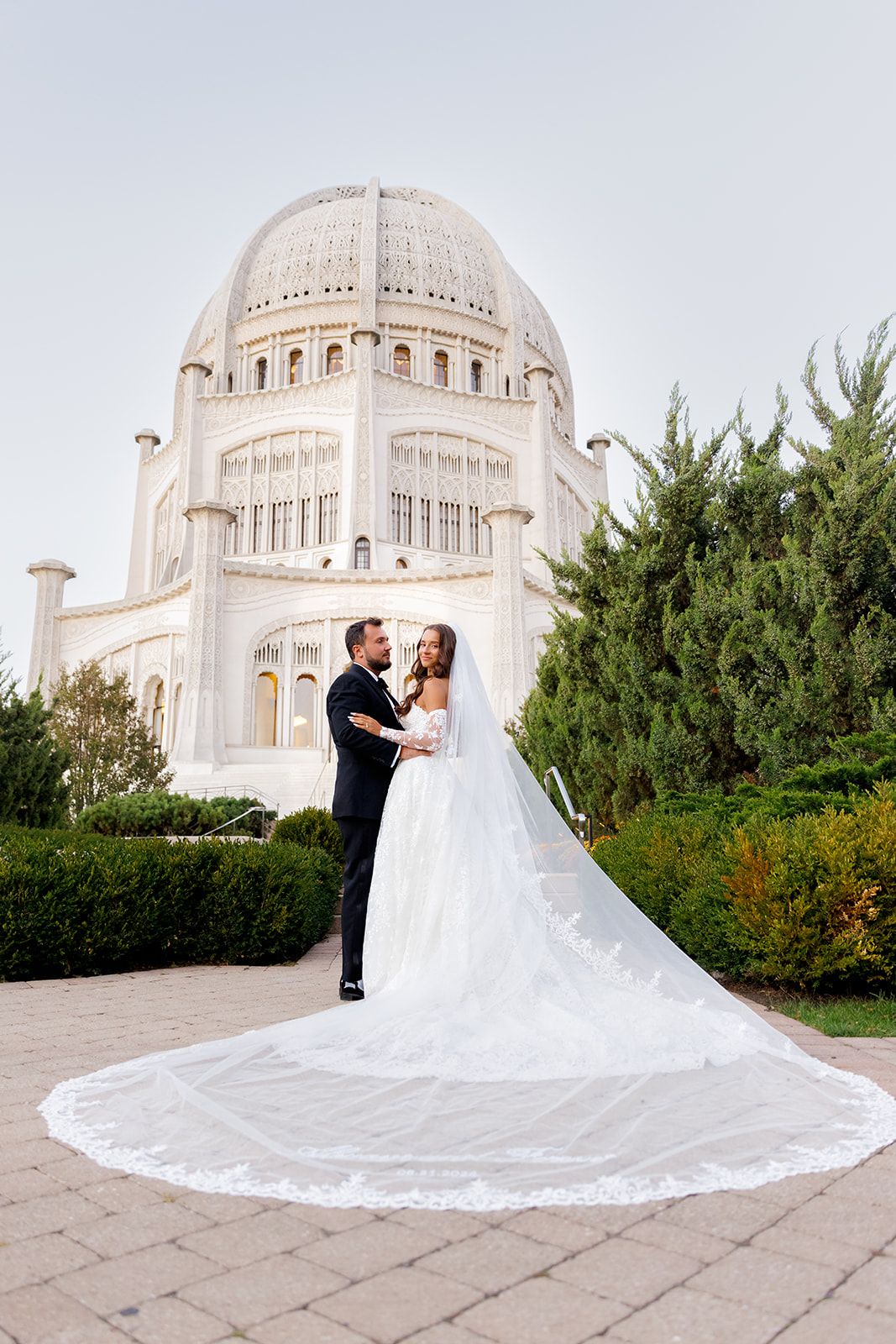 Bride and groom embrace in front of the Bahá'í Temple in Wilmette, Illinois, with a flowing cathedral veil.