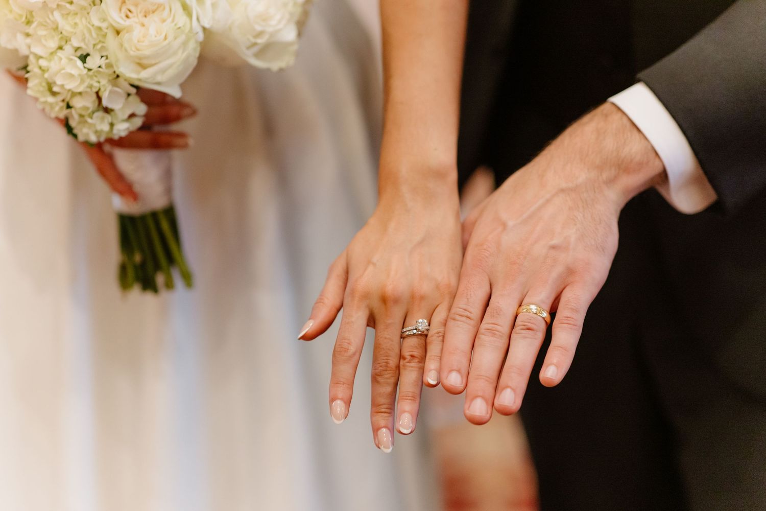 Newlyweds display wedding rings beside white bridal bouquet after ceremony.