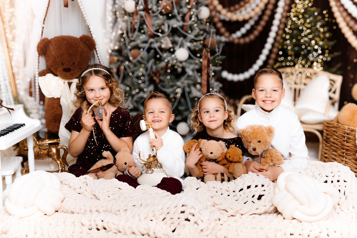 Four children pose with teddy bears near a decorated Christmas tree in a festive holiday photo session.