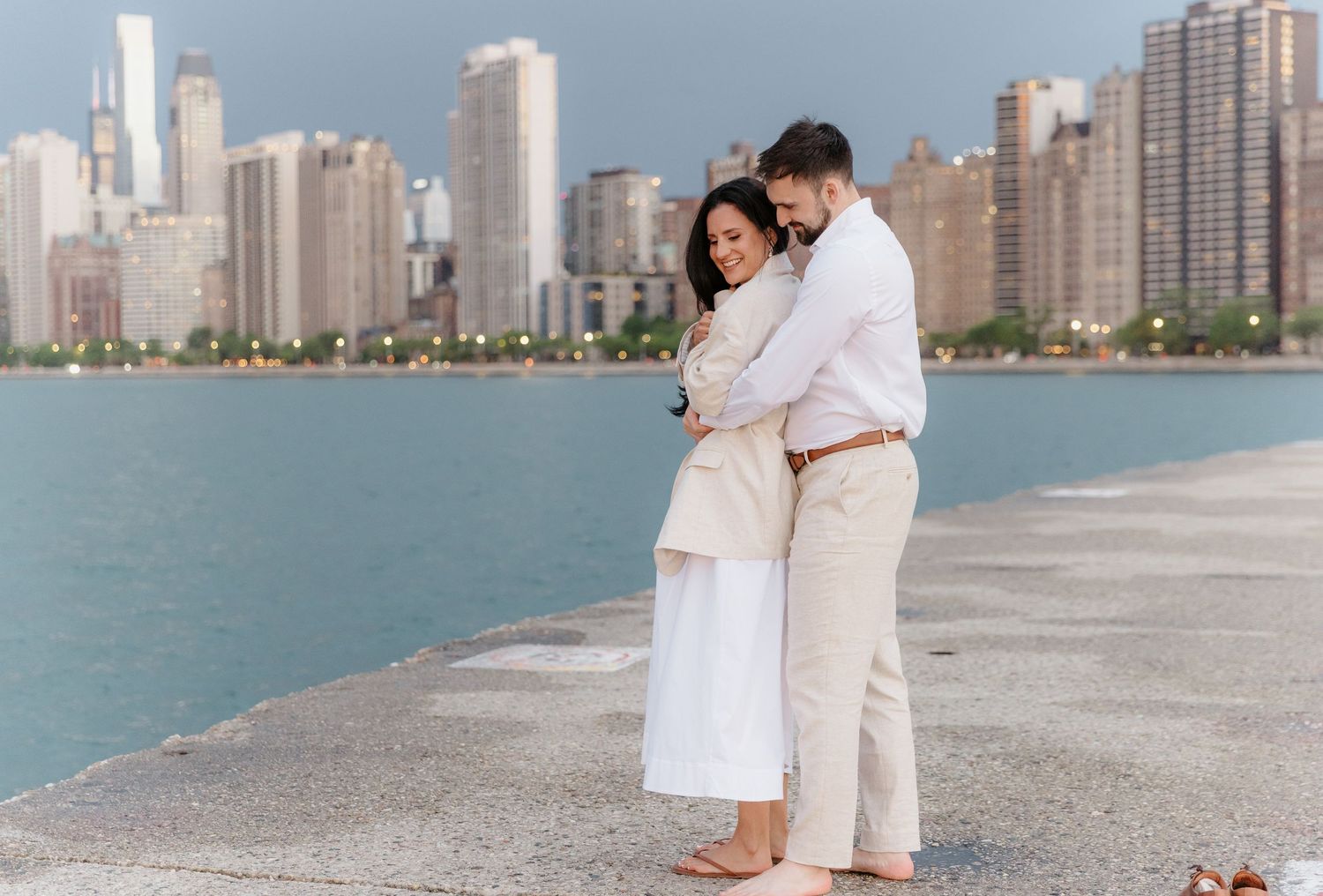 Couple embracing tenderly on Chicago lakefront pier with blue water and skyline behind them.