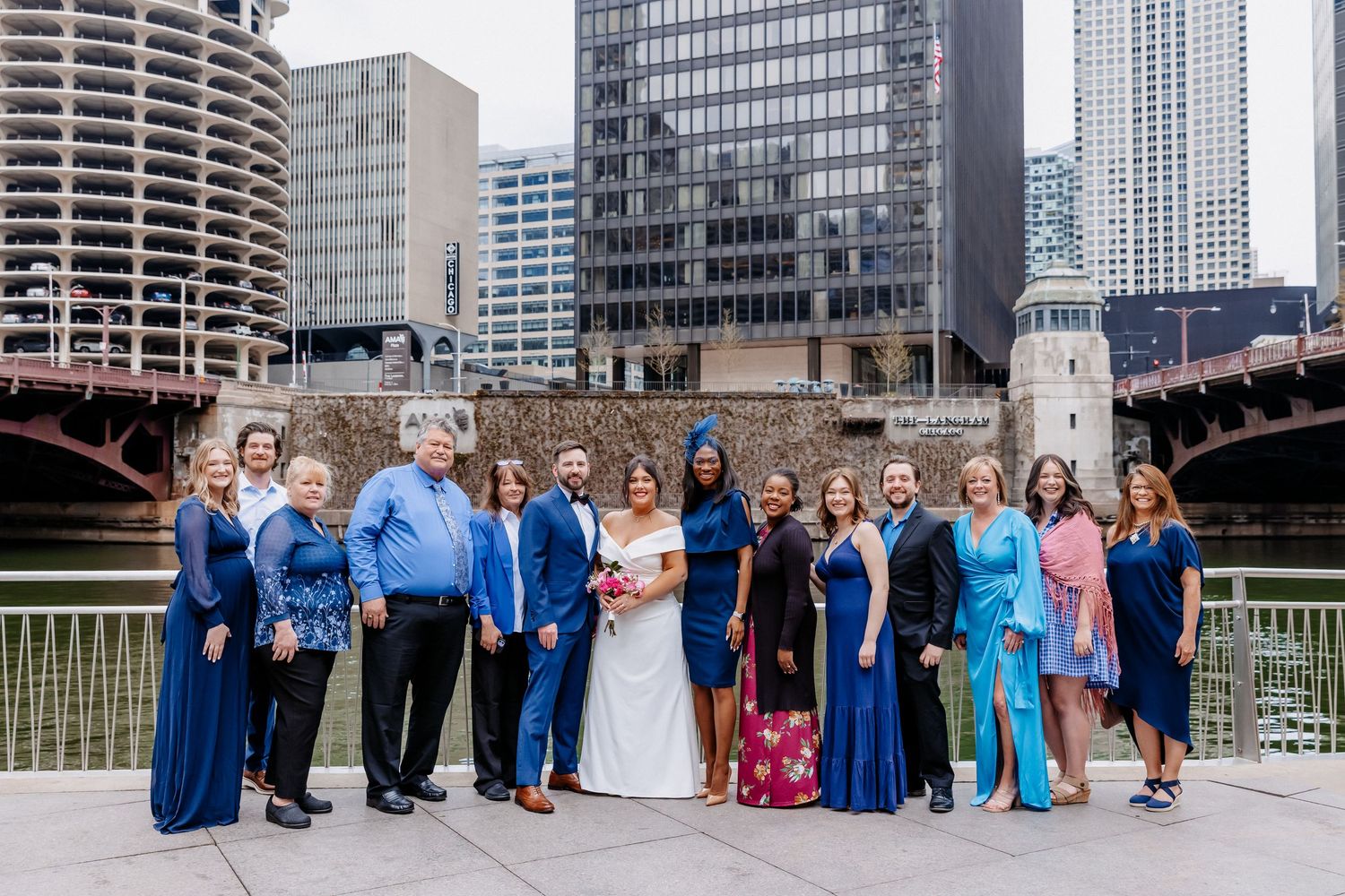 Large wedding party poses together in blue attire with bride and groom on Chicago Riverwalk.