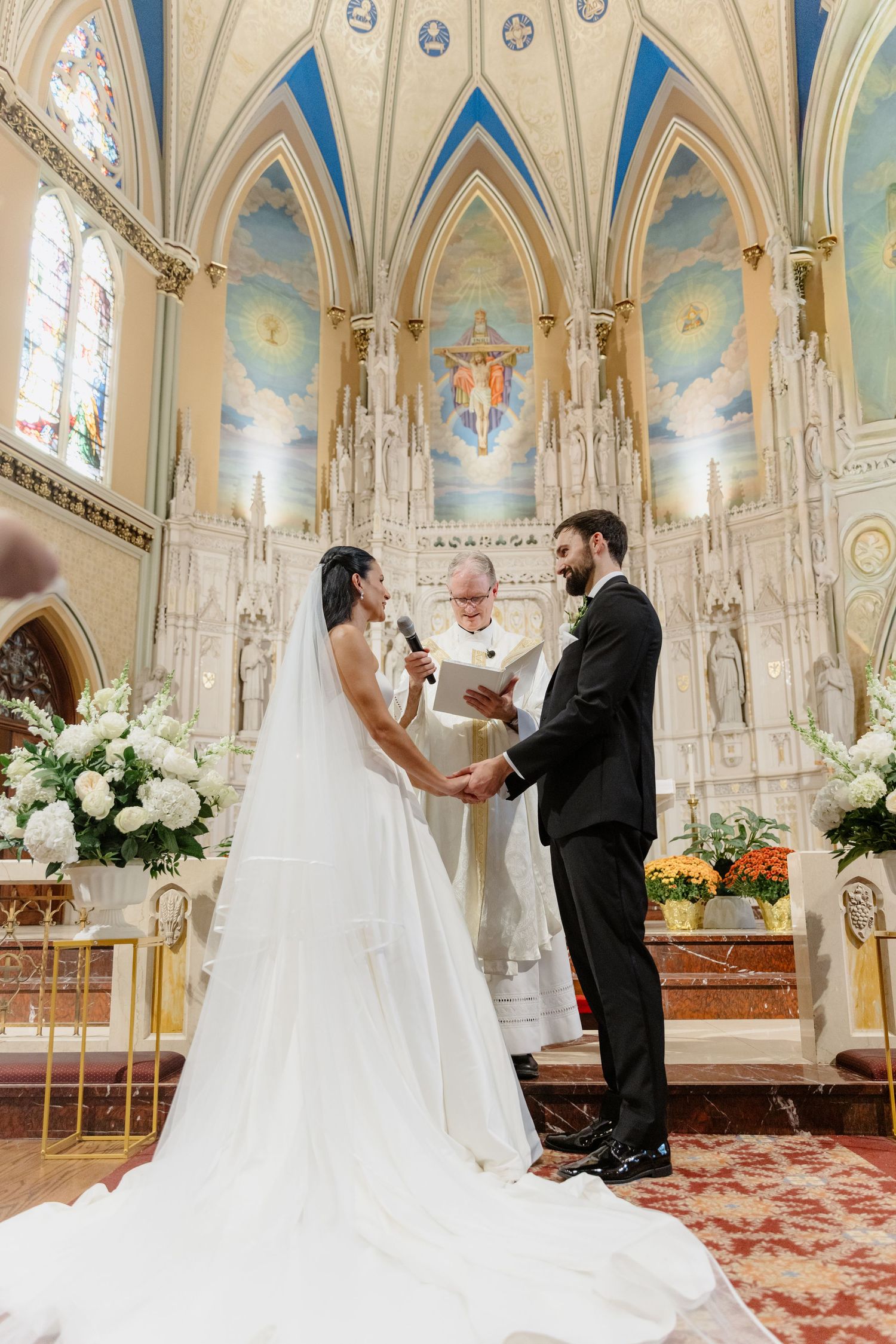 Bride and groom exchange vows at ornate cathedral altar with stunning blue painted ceiling.