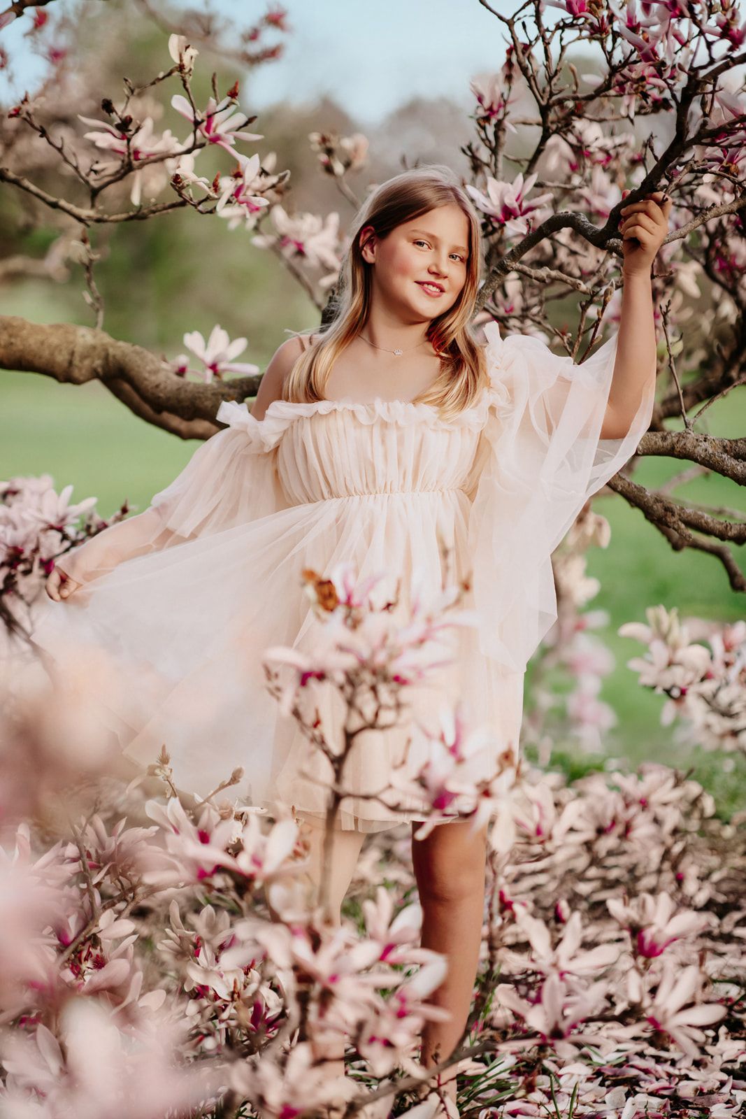 Young girl in white dress among blooming pink magnolia trees in spring garden.