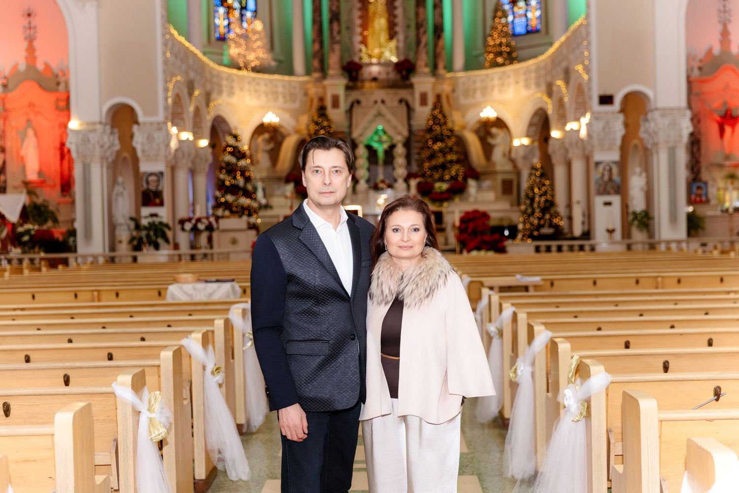 Couple in formal attire posing together in beautifully decorated church with Christmas decorations.