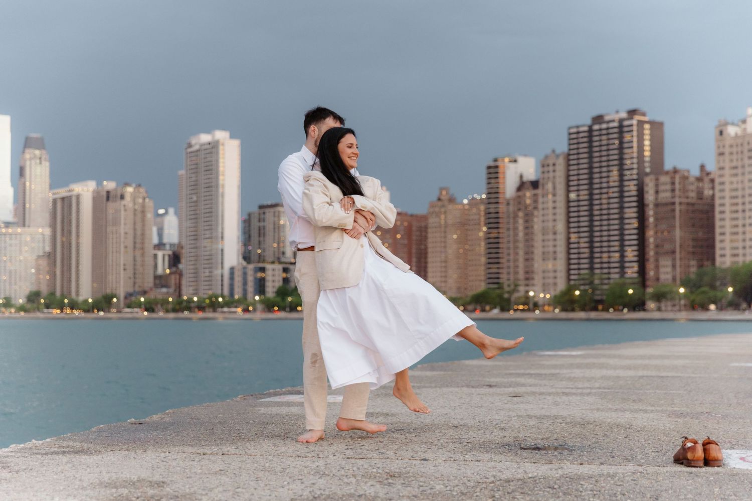Playful couple spinning on Chicago lakefront pier with city skyline and lake in background.