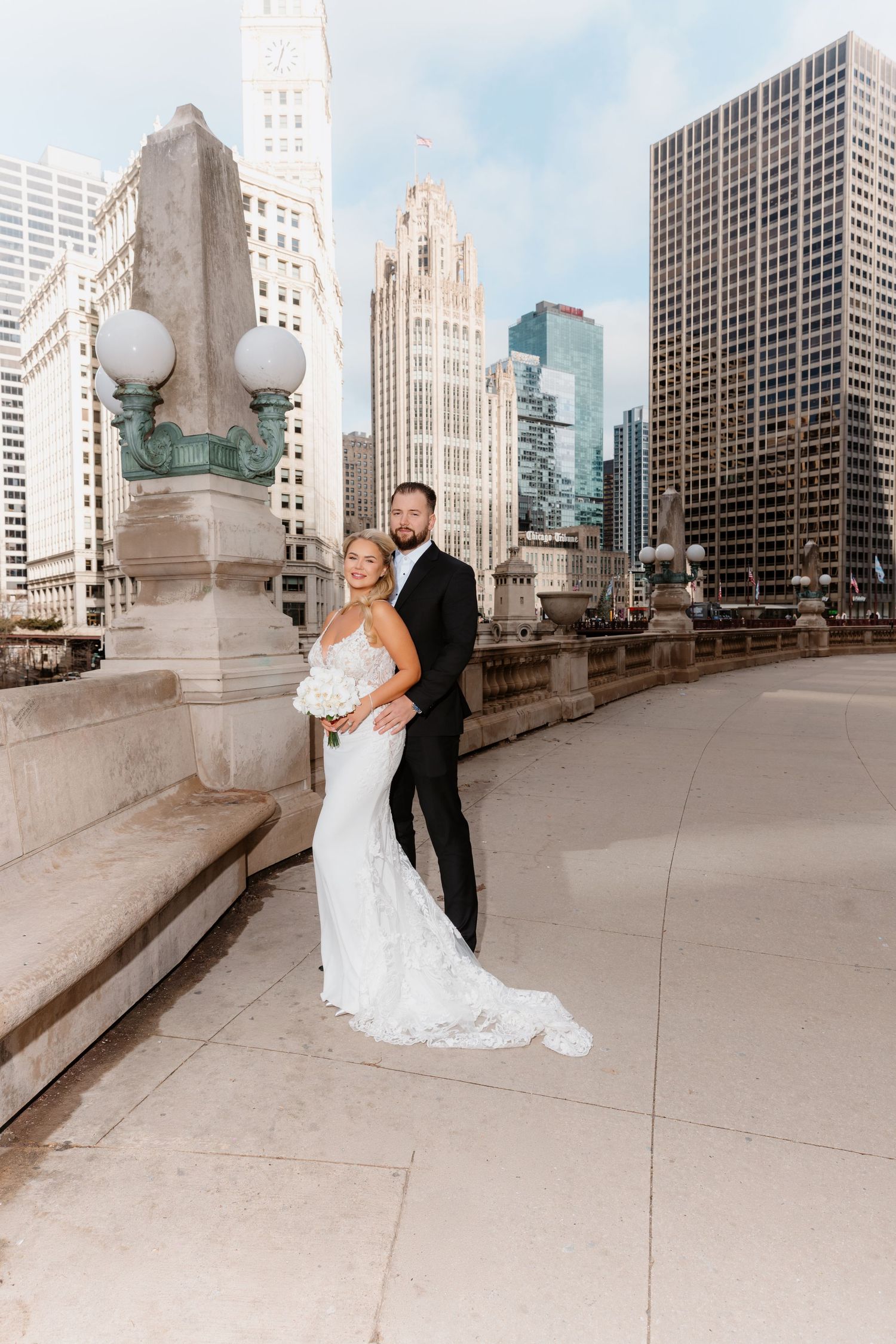 Wedding couple poses on Chicago DuSable Bridge with Tribune Tower and city skyscrapers in background.
