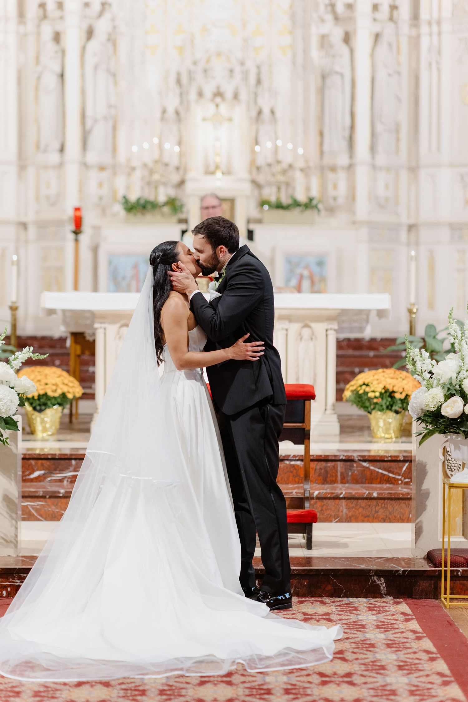 Bride and groom share first kiss at ornate white church altar after ceremony.