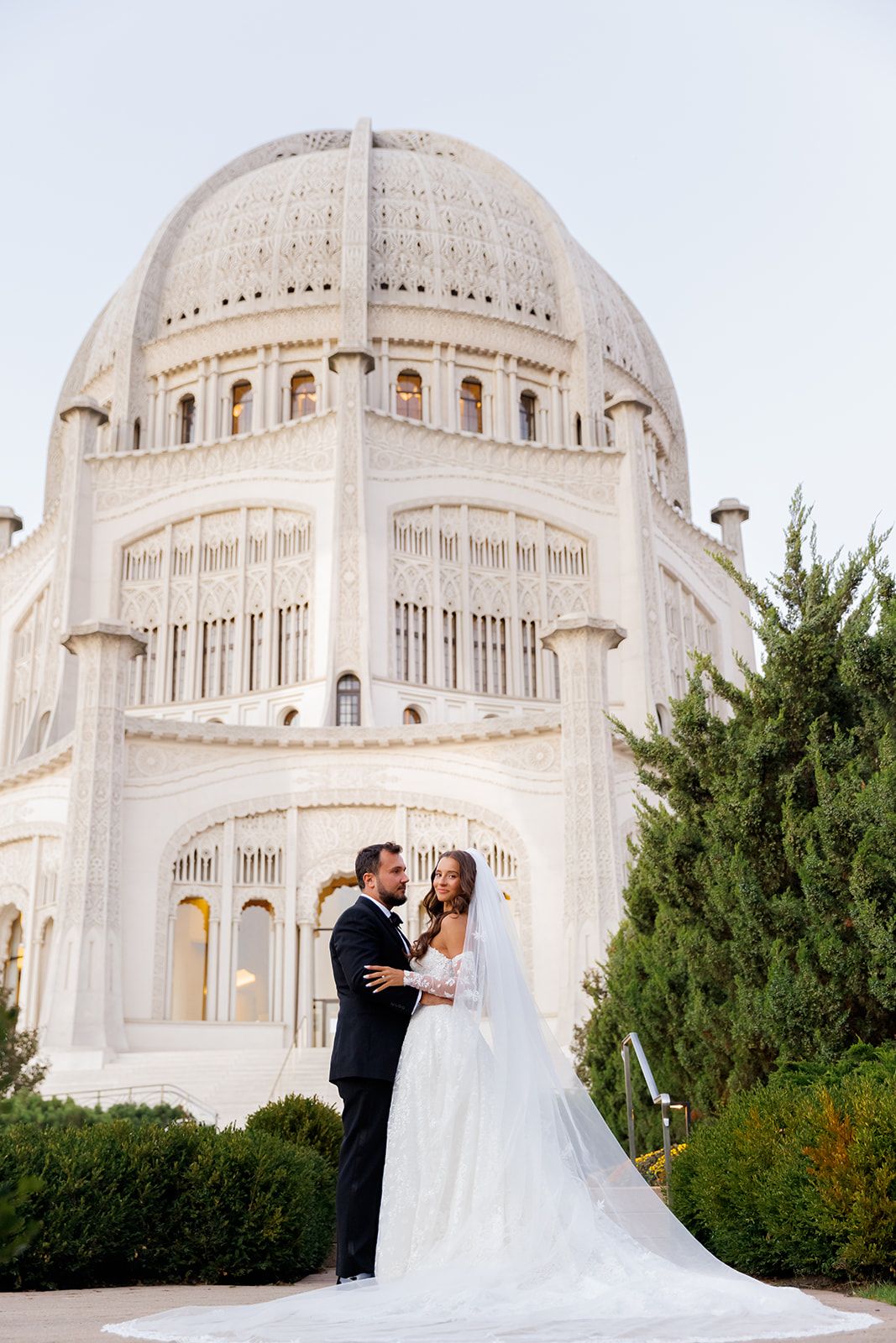 Bride and groom embrace in front of the ornate white Bahai Temple dome in Wilmette, Illinois.