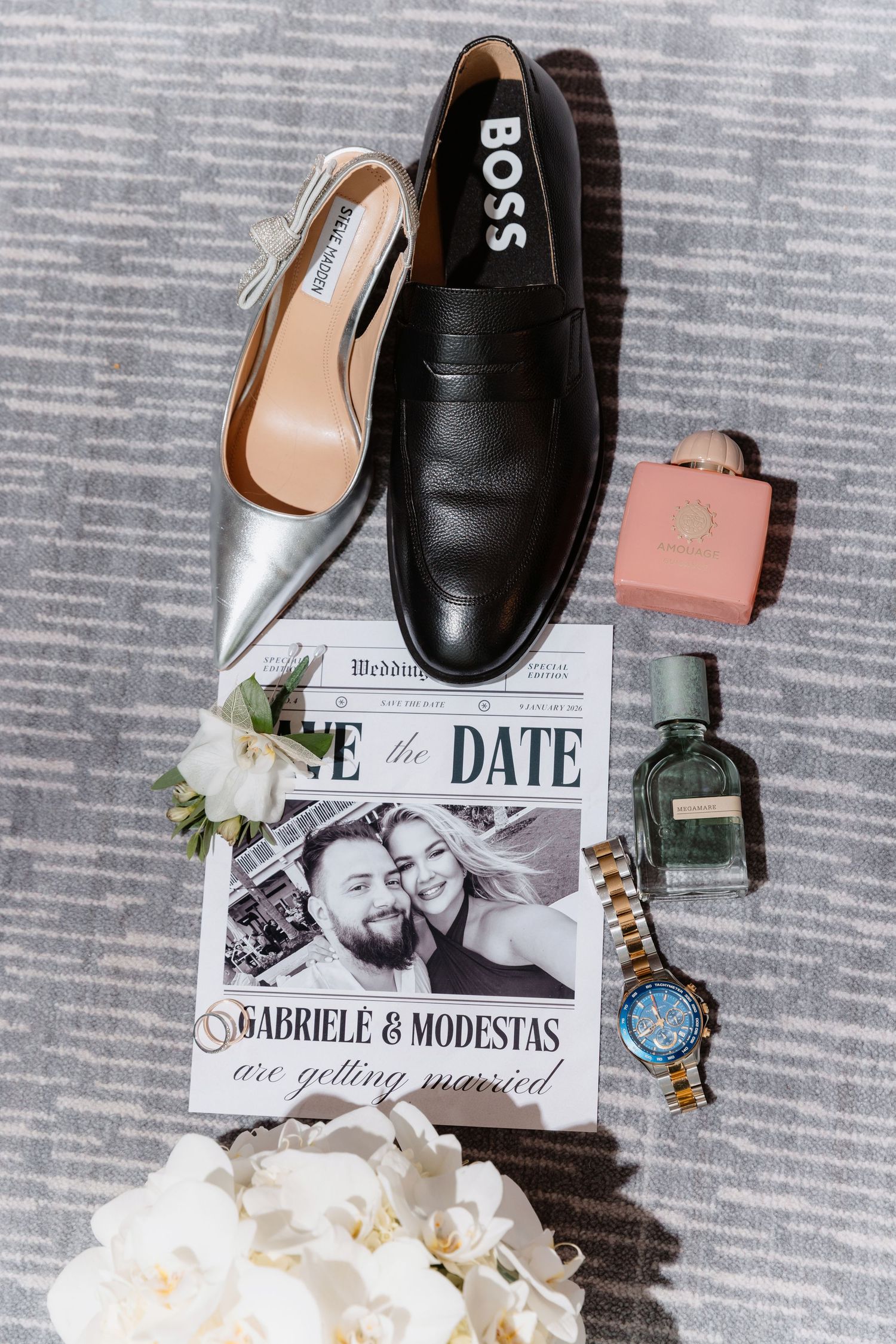 Wedding flat lay featuring BOSS loafer, silver heels, save the date, perfume, pink box, and watch.