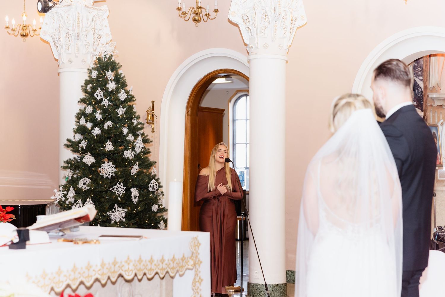 Female vocalist performing near Christmas tree during elegant church wedding ceremony.