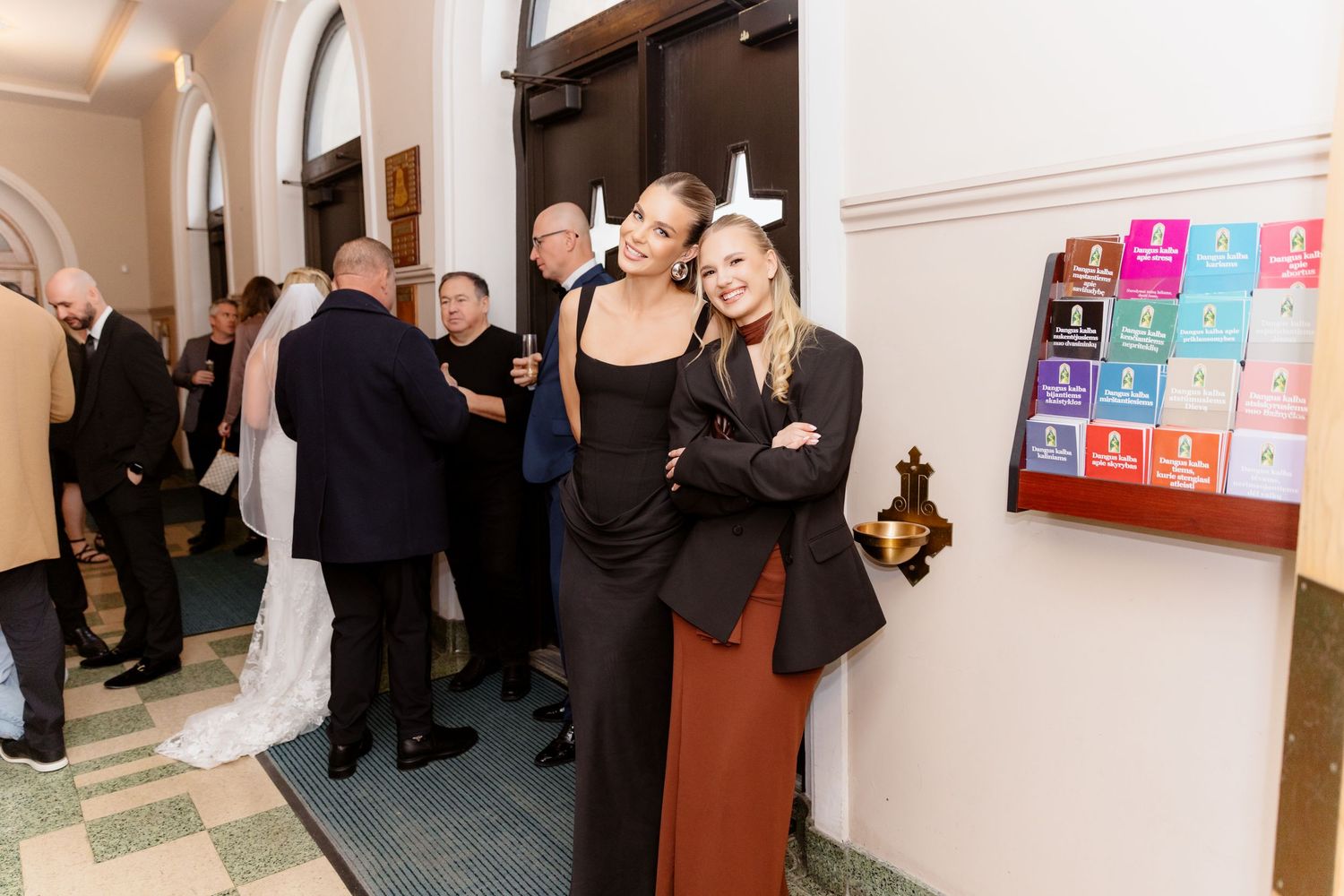 Two blonde women posing together at upscale formal event with guests.