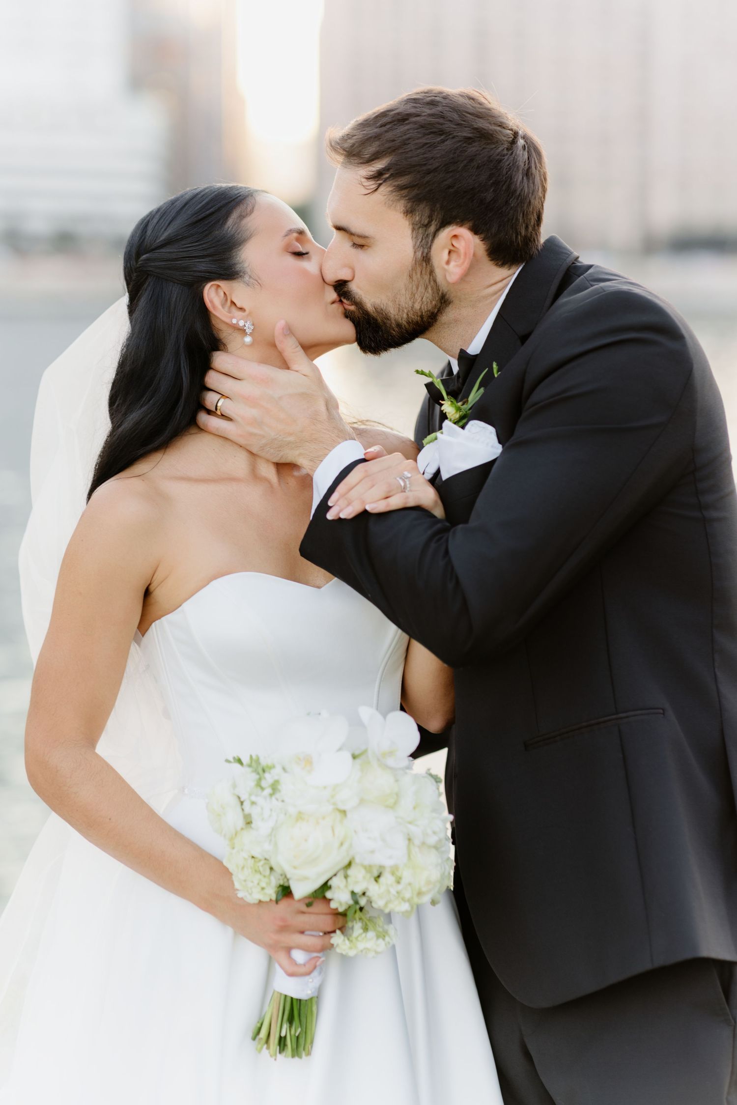 Bride and groom sharing romantic kiss, bride holding white floral bouquet.