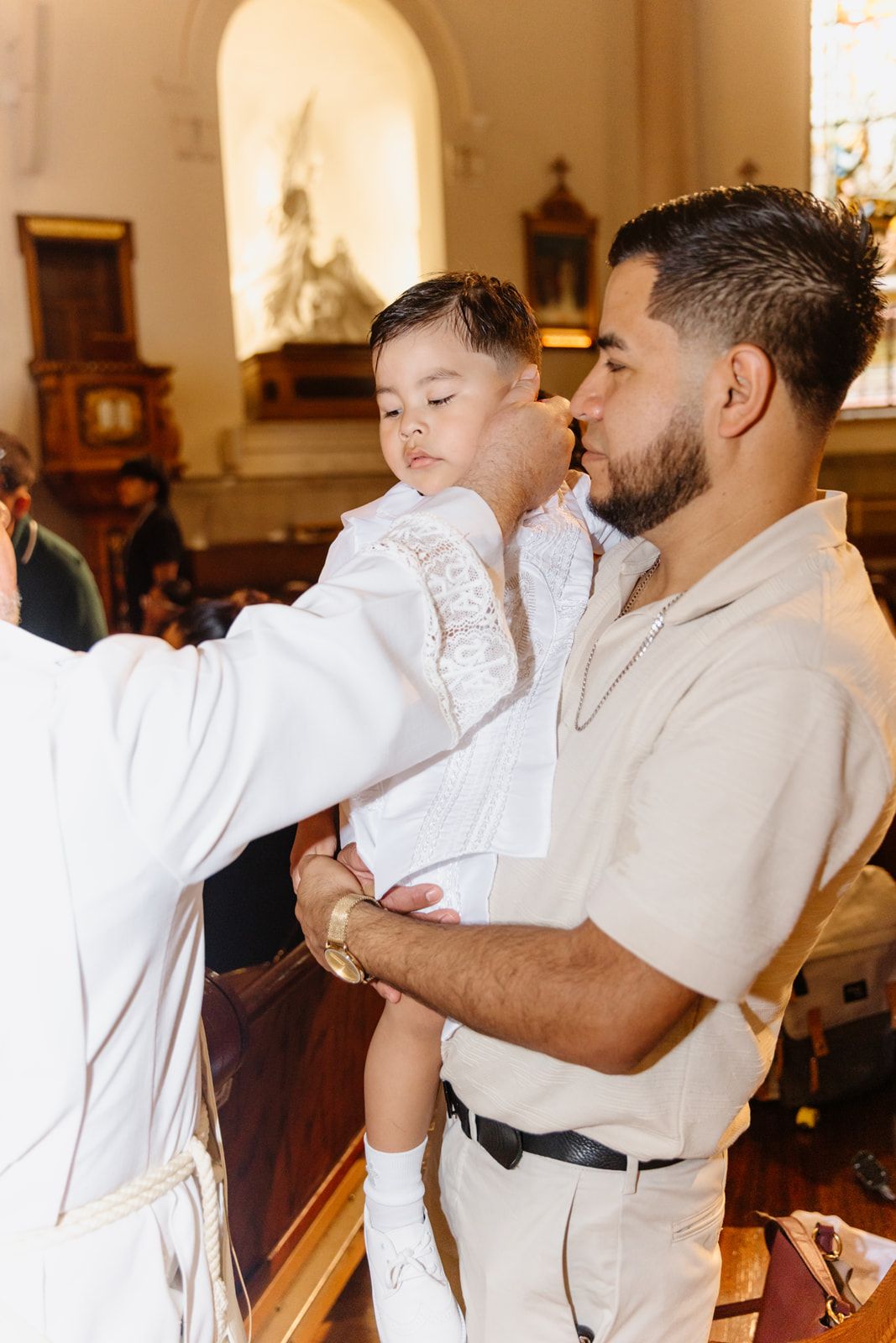 Priest anointing a baby boy held by his father during a Catholic baptism.