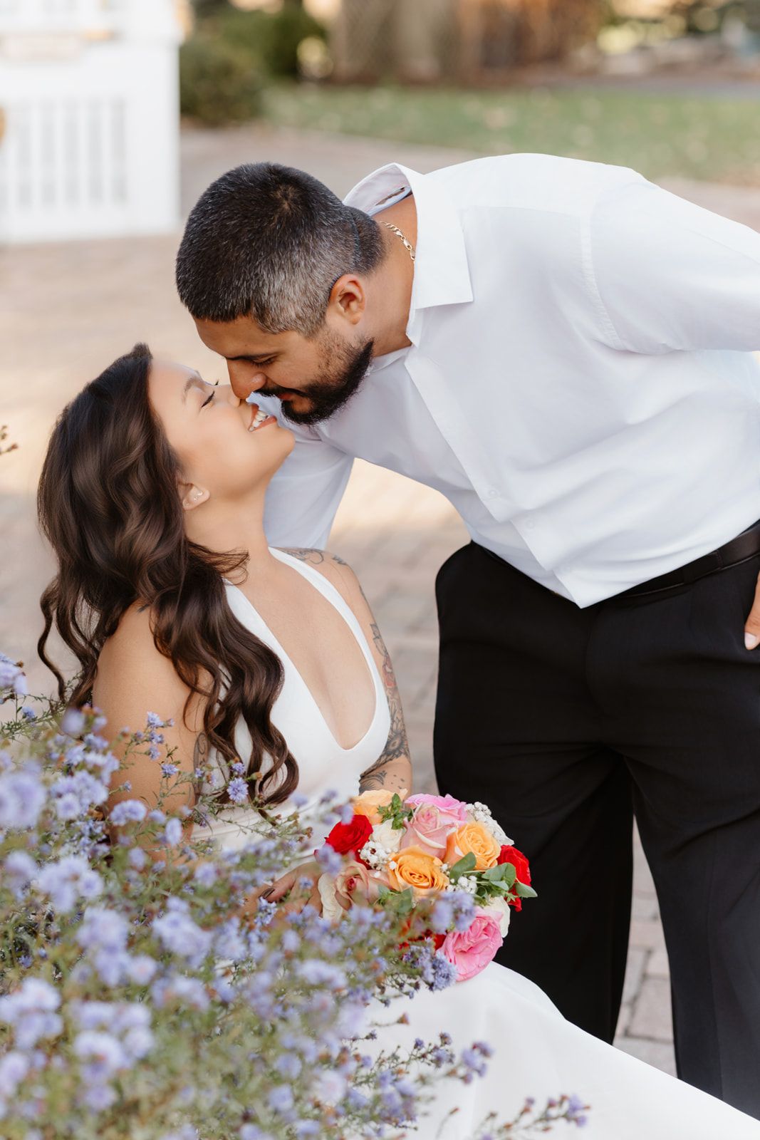 Bride and groom share a romantic kiss surrounded by purple wildflowers, bride holding vibrant colorful bouquet.