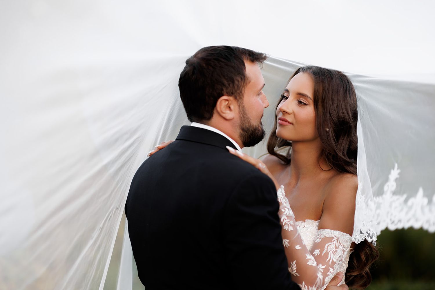 Bride and groom share a romantic moment under a flowing white wedding veil.