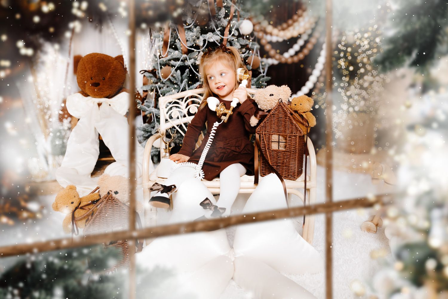 Young girl in brown dress holds teddy bears near decorated Christmas tree with snow effect.