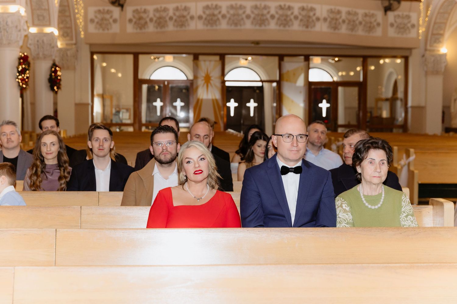 Elegantly dressed wedding guests seated in wooden church pews during ceremony.