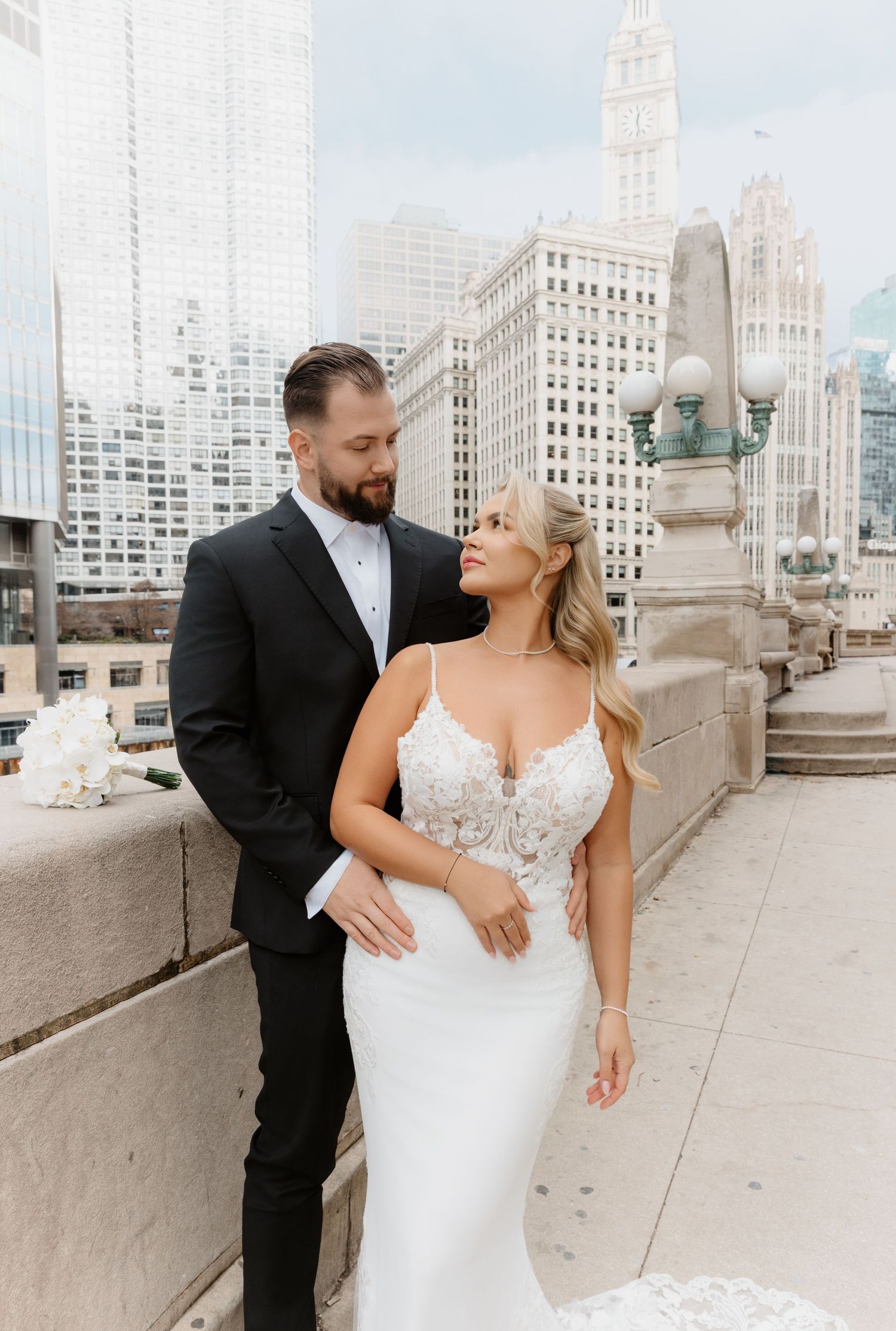 Bride and groom posing romantically on rooftop terrace with Chicago city skyline in background.