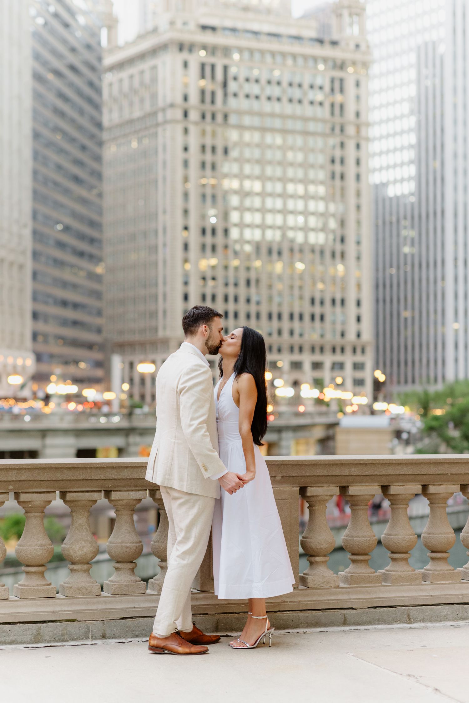 Couple kissing on Chicago riverwalk terrace with stunning city skyscraper backdrop at golden hour.