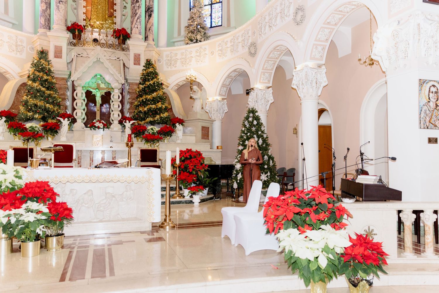 Elegant church interior decorated with Christmas trees and red poinsettias around the altar.