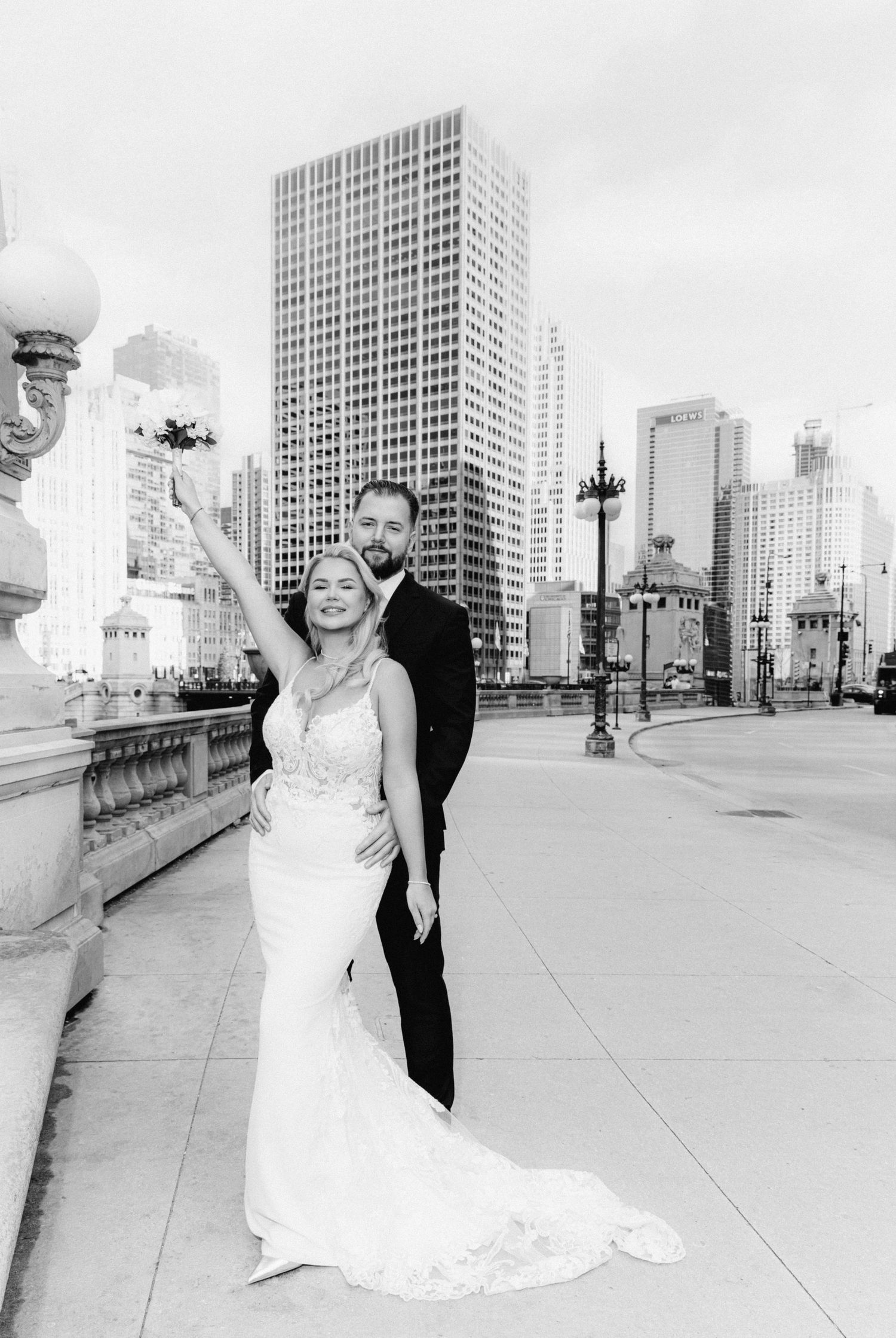 Black and white photo of a bride and groom posing in front of a city skyline on their wedding day.