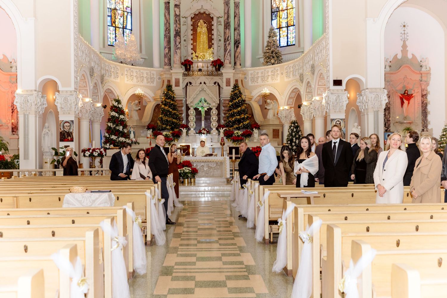 Wedding party gathered at decorated church altar with Christmas trees and white floral arrangements.