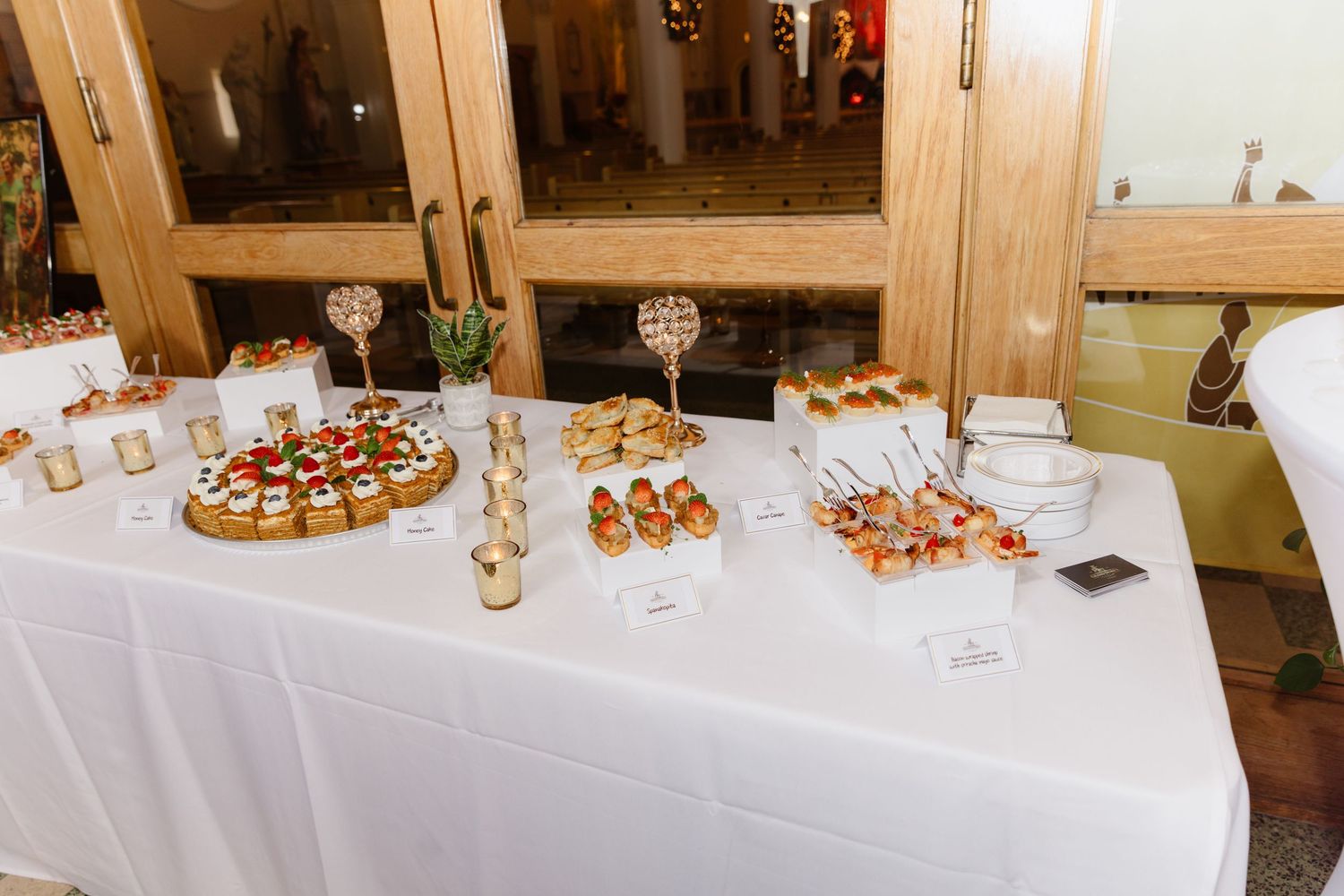 Wedding cocktail hour display table featuring assorted finger foods and appetizers on a white linen tablecloth.