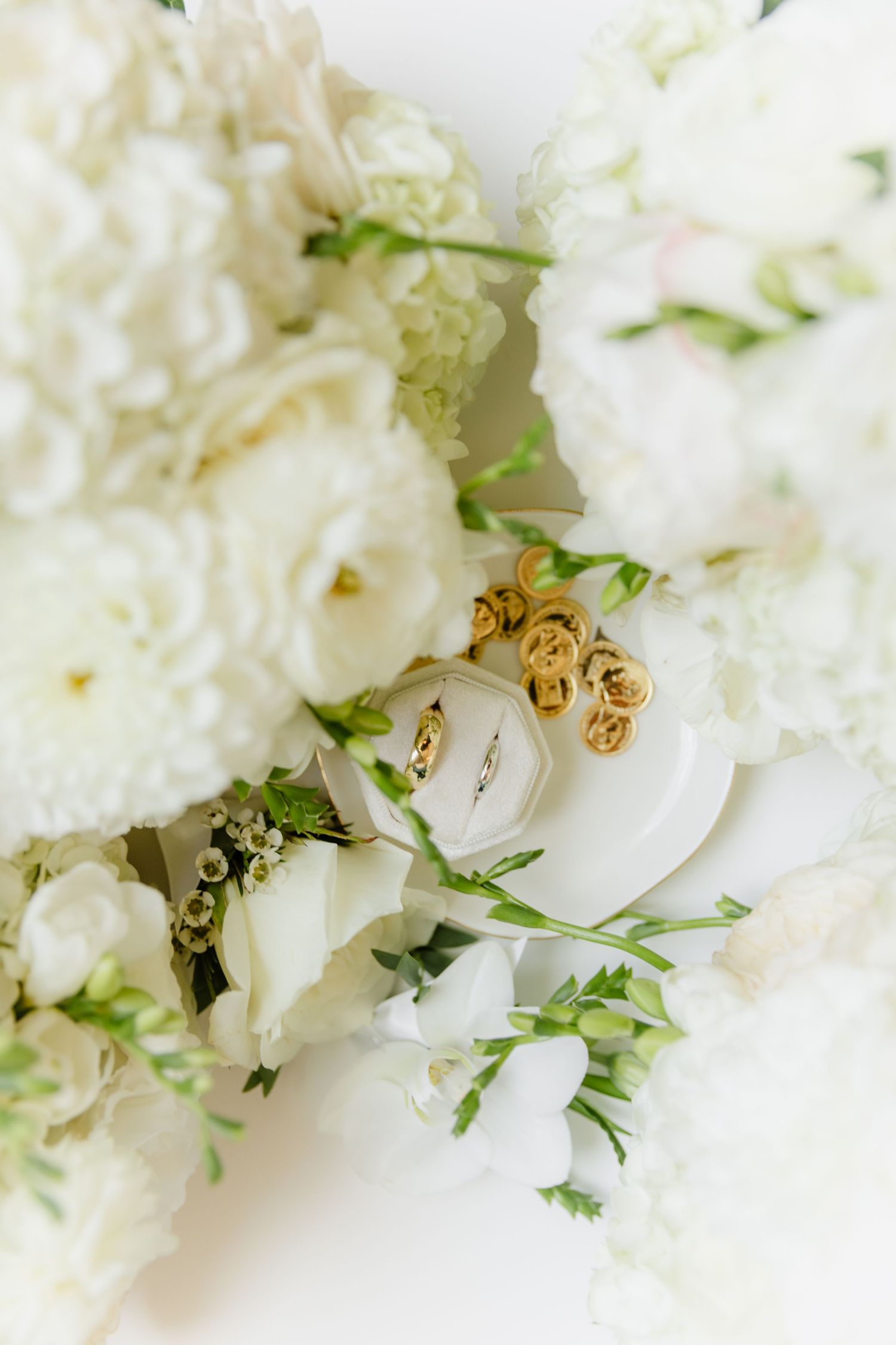 Close-up of white floral bouquet with diamond ring in white box and gold rose earrings.
