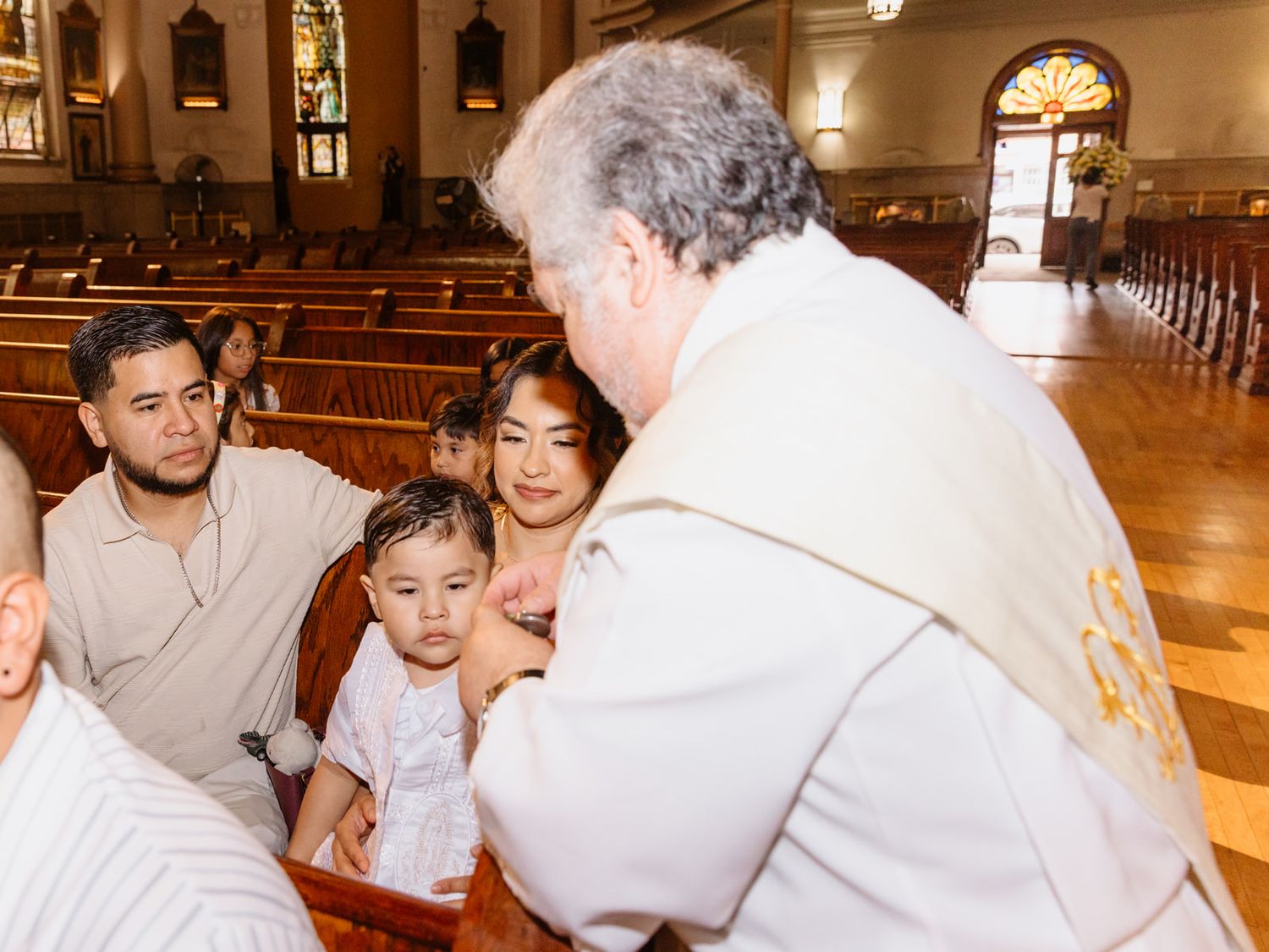 Priest blesses a young child held by mother during a Catholic baptism ceremony in a church.