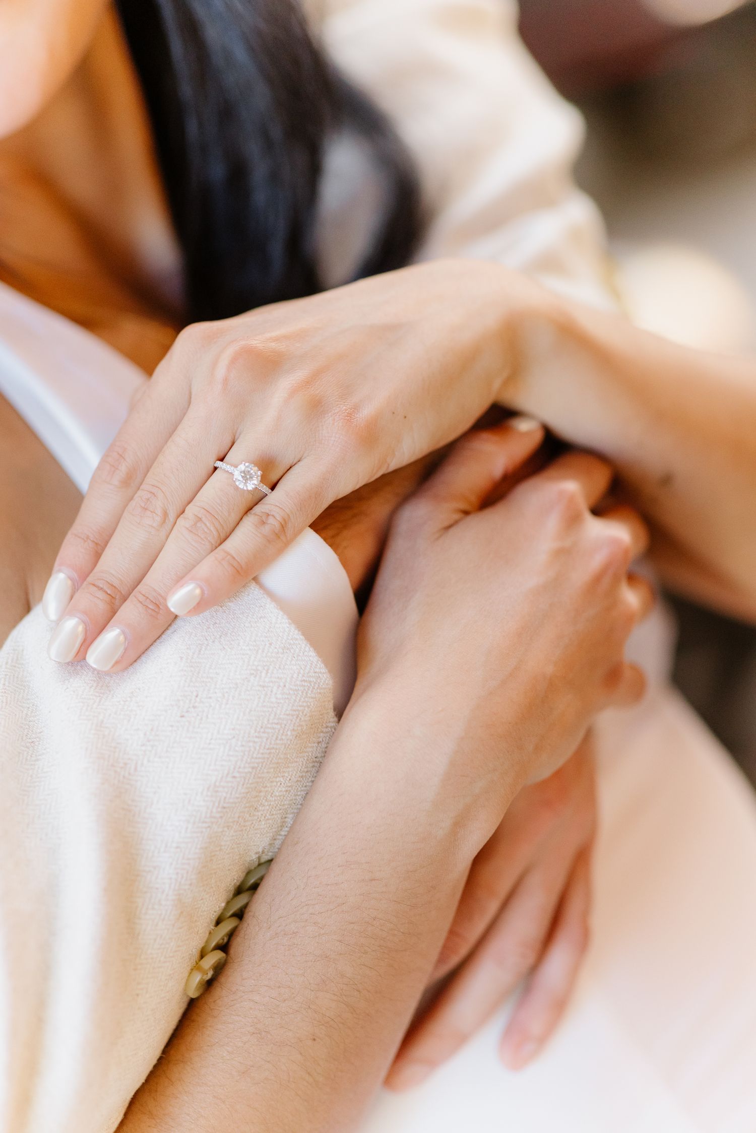 Close-up of woman's hand wearing a diamond engagement ring resting on man's arm.