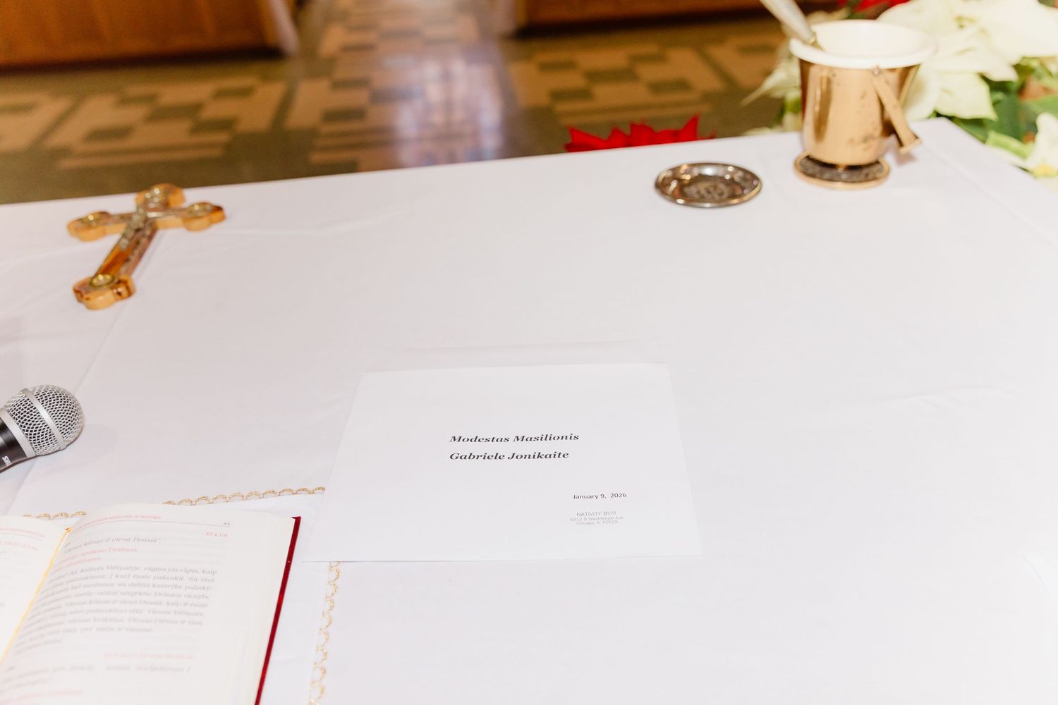 White altar table with a gold cross, microphone, and printed ceremony program card on top.