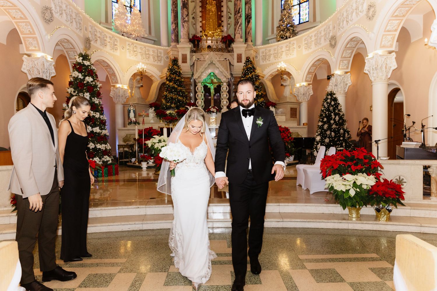 Newlyweds walk hand-in-hand down the aisle of a Christmas-decorated church after their wedding ceremony.