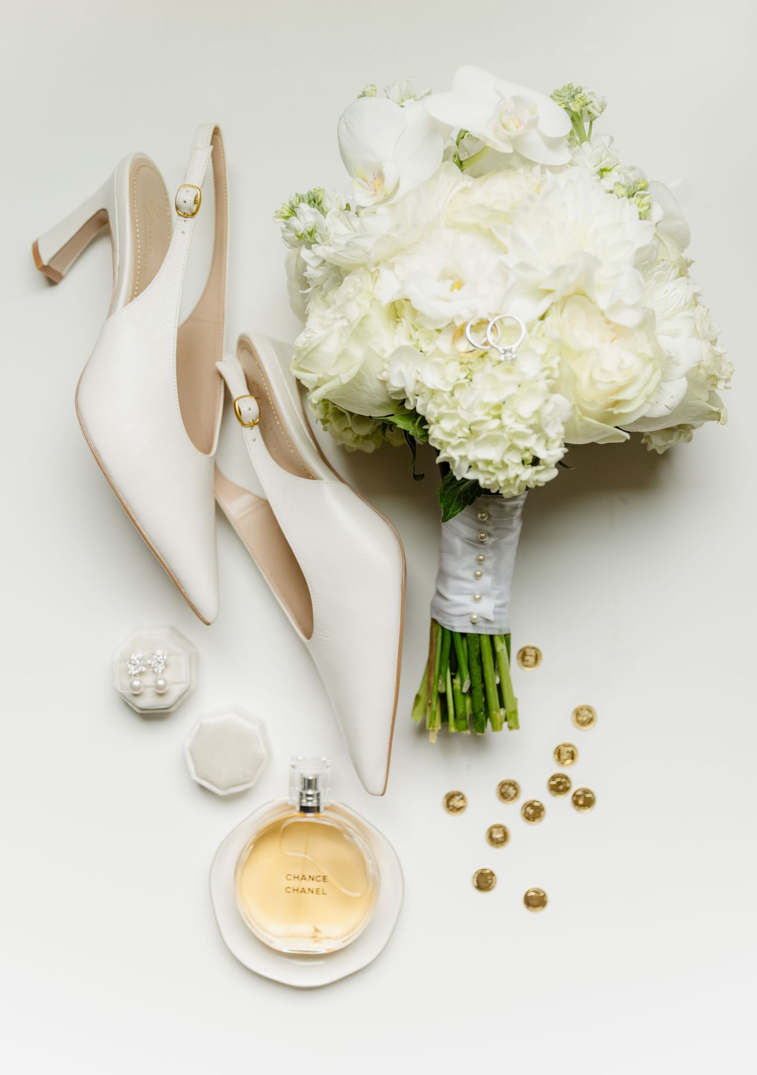 Bridal flat lay with white heels, white flower bouquet, Chanel perfume, and gold accessories.