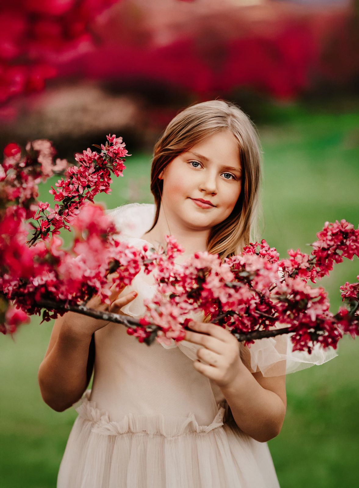 Young girl in white dress holding pink cherry blossom branches in a garden.