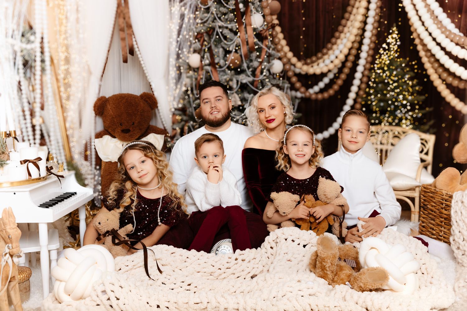 Family of five poses for festive Christmas portrait with decorated tree, teddy bears, and holiday decor.