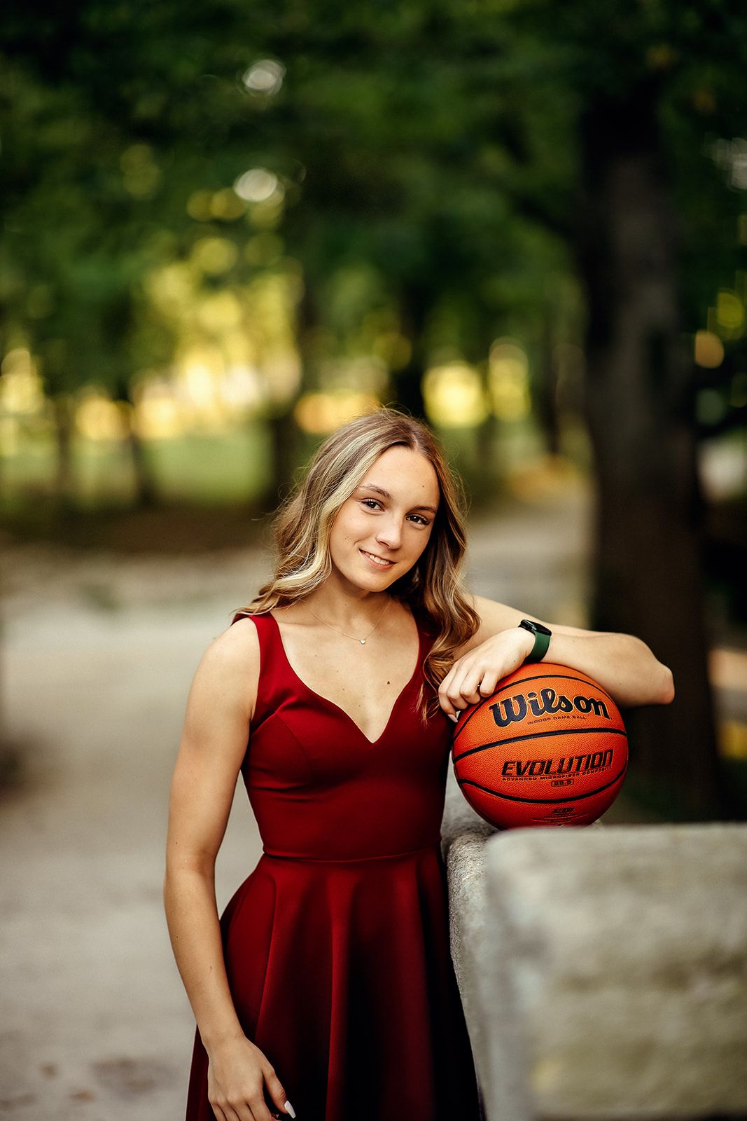 Smiling young woman in red dress holds a Wilson Evolution basketball while posing outdoors.