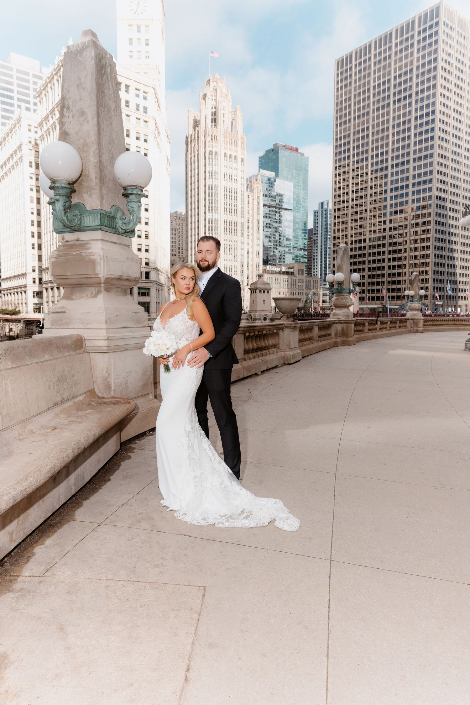 Bride and groom pose elegantly on Chicago bridge with iconic city skyline in background.