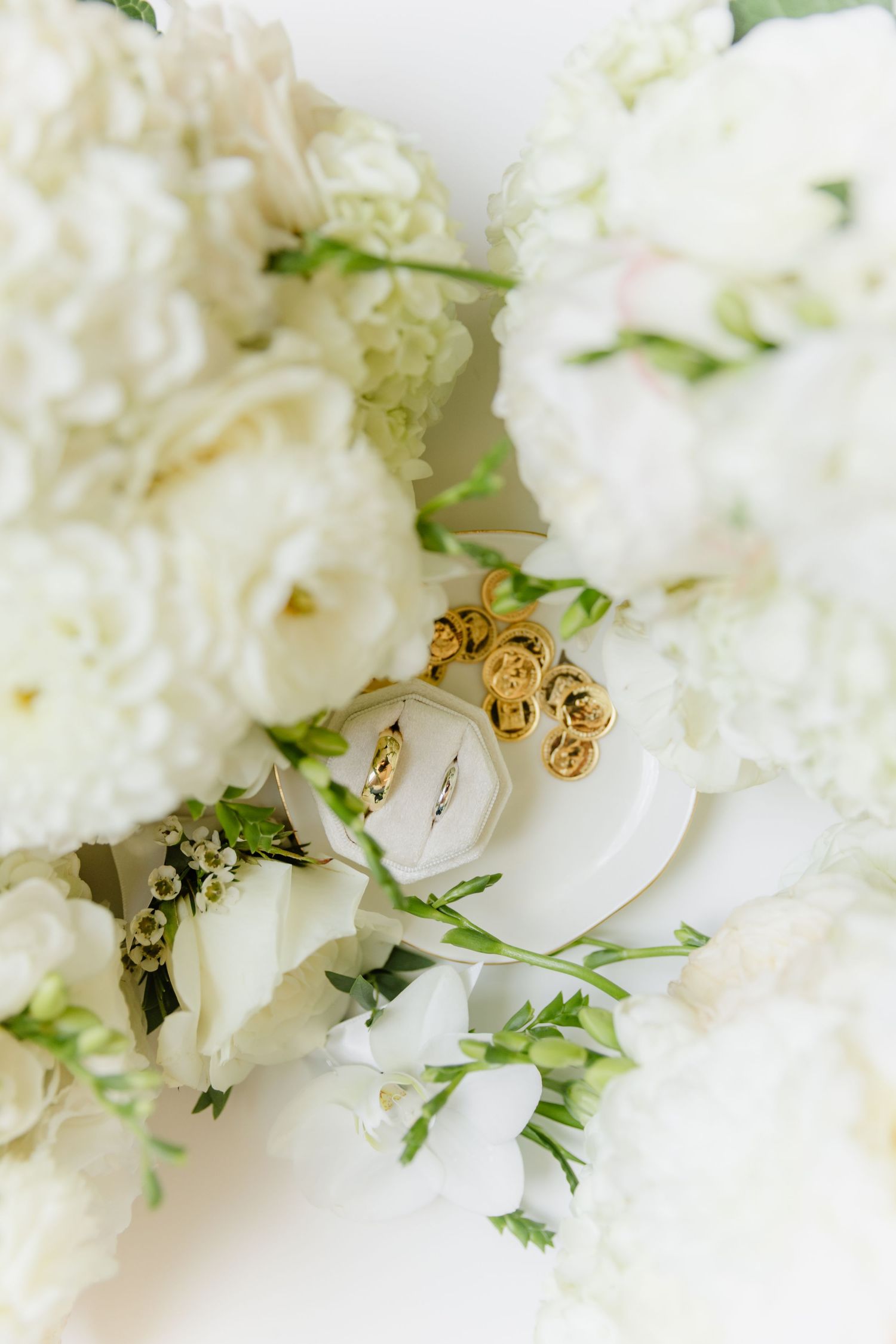 White wedding bouquet with roses and hydrangeas, featuring gold rose earrings and a diamond ring nestled among the blooms.