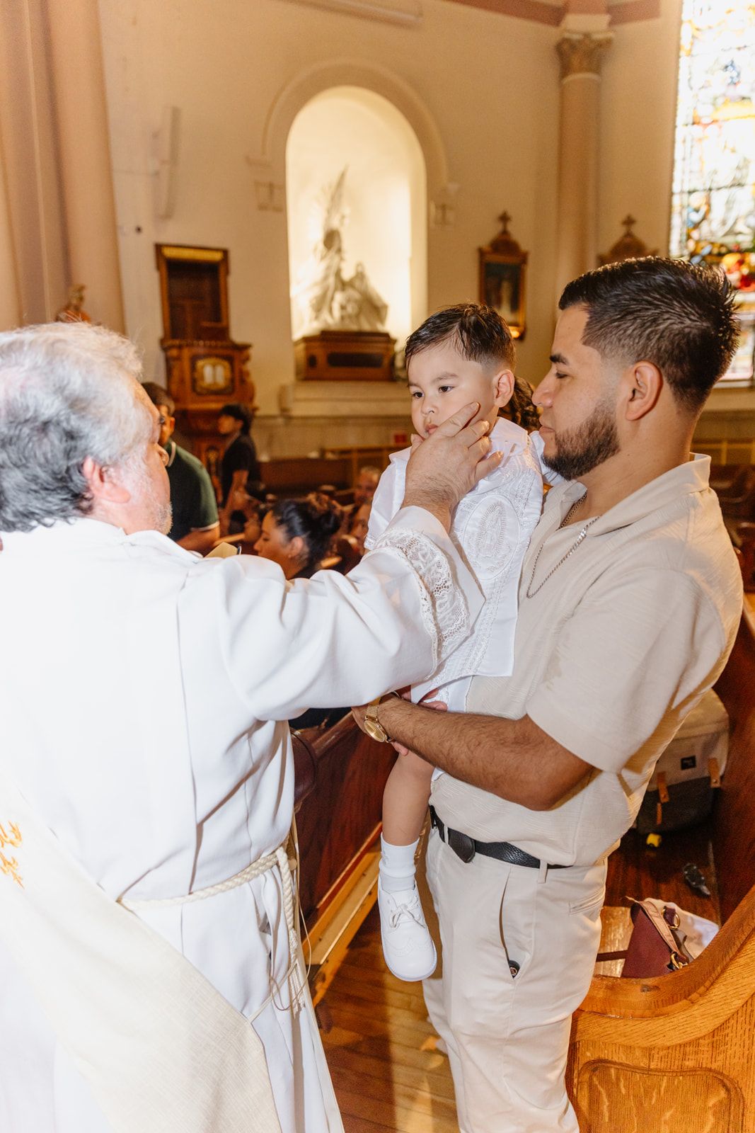 Catholic priest blessing a young child held by his father during a baptism ceremony.
