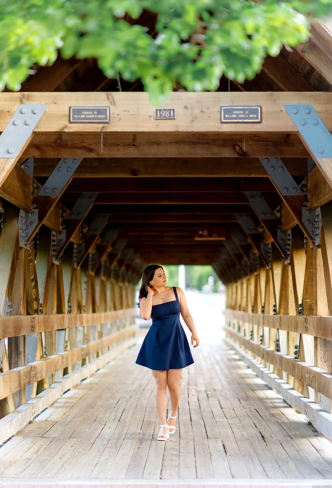 Young woman in navy mini dress walking through a rustic wooden covered bridge.