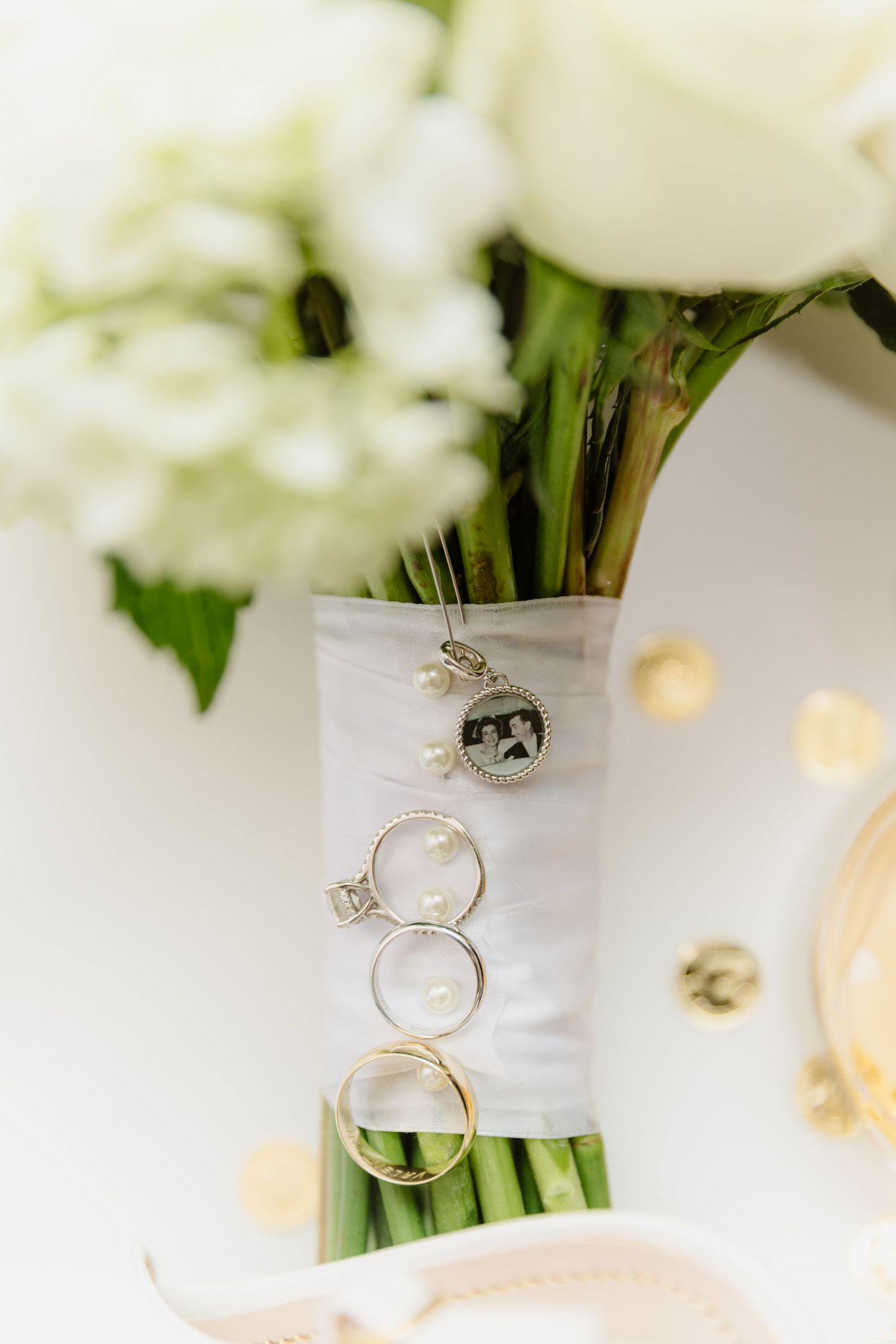 Wedding rings and diamond engagement ring displayed on white bouquet ribbon with memorial photo charm.