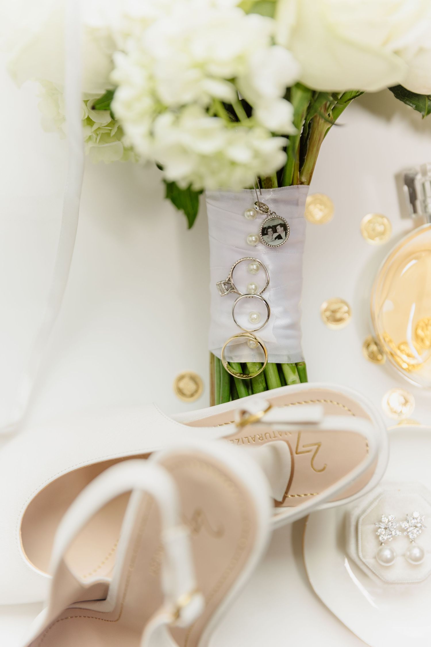 Elegant bridal detail flat lay with white bouquet, nude heels, wedding rings, and gold accents.