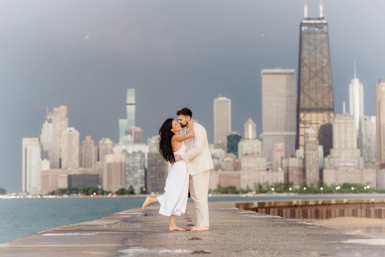 Romantic couple embracing and kissing on Chicago waterfront pier with iconic city skyline behind them.