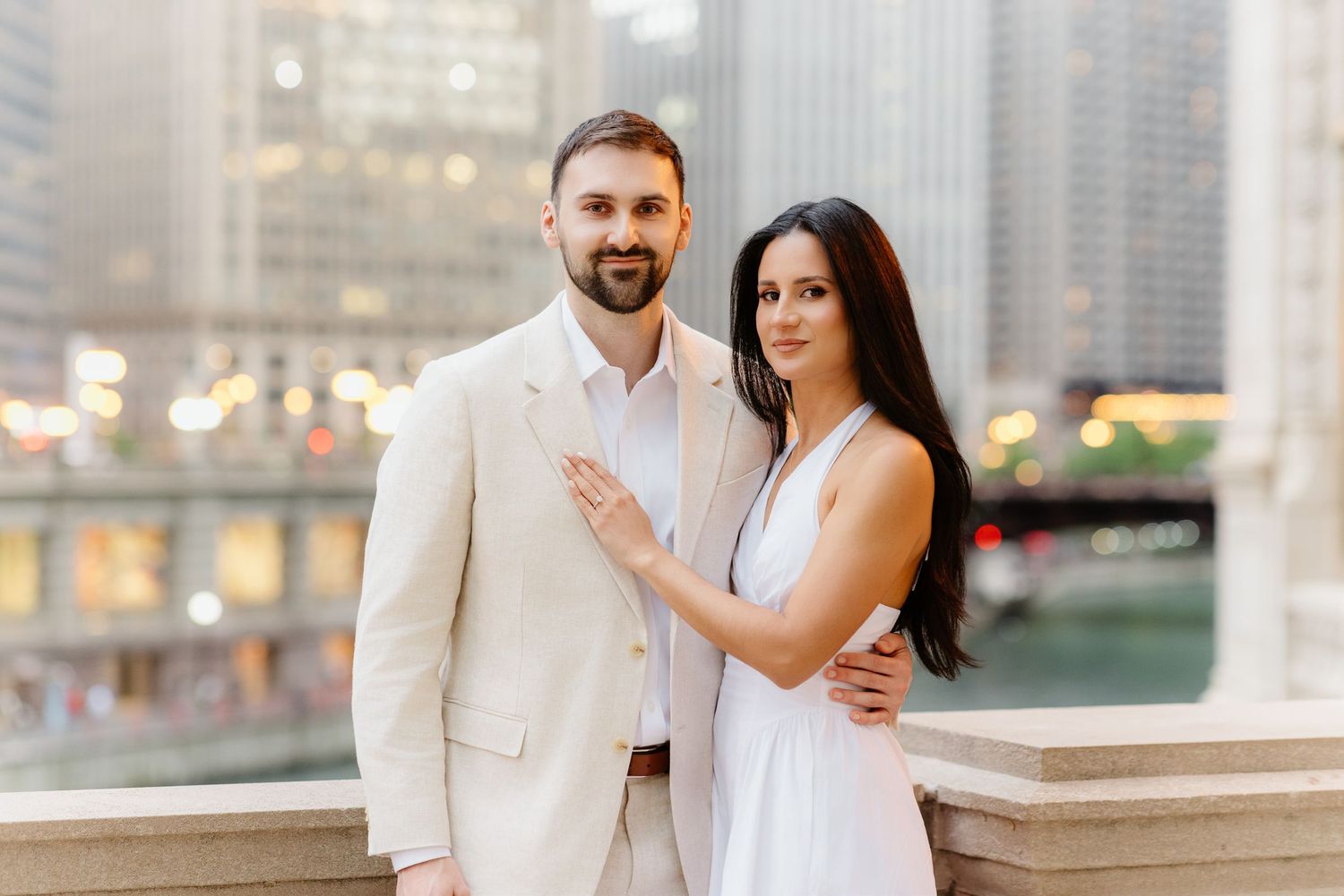 Engaged couple posing together on a bridge with Chicago city skyline and bokeh lights behind them.