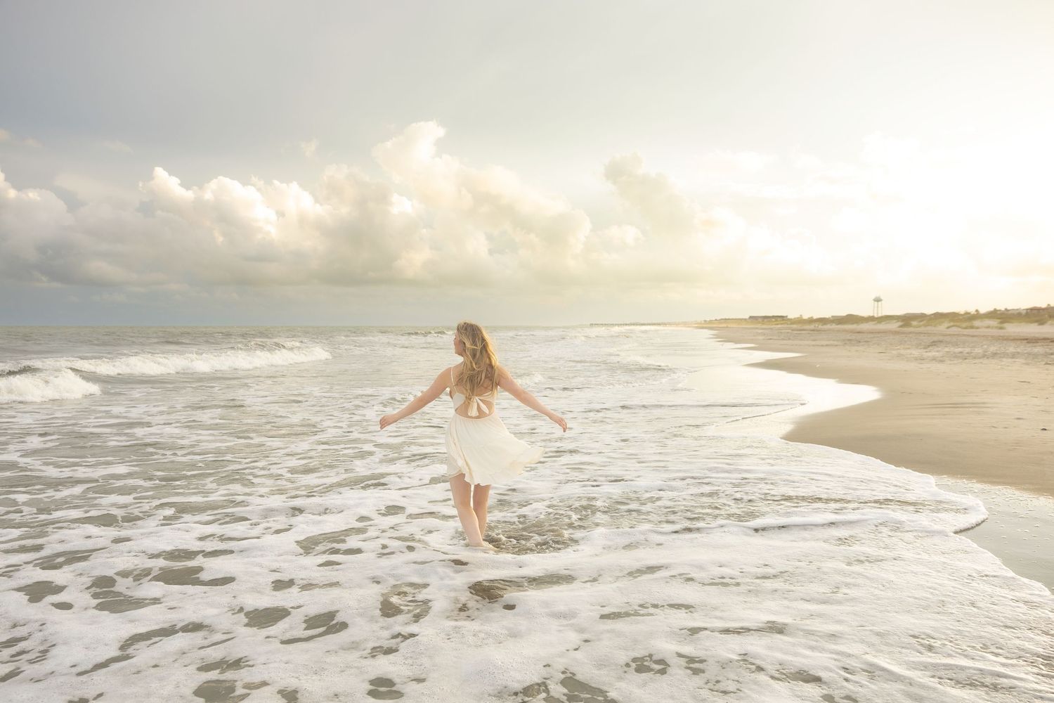 Woman in white dress walking into ocean waves on a sunlit beach at golden hour on Isle of Palms.