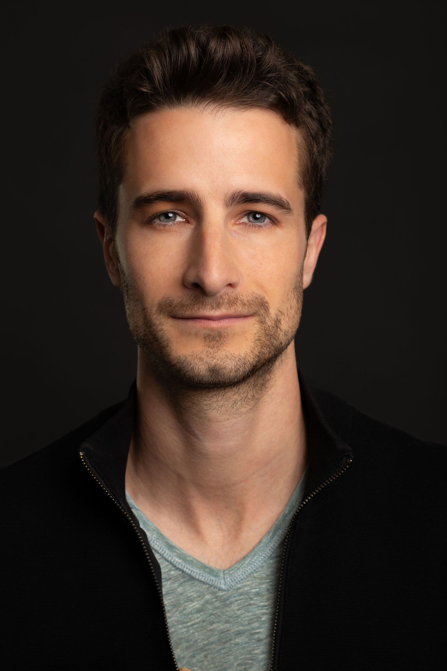 Young CEO with blue eyes poses for professional headshot on dark background in Charleston, SC.