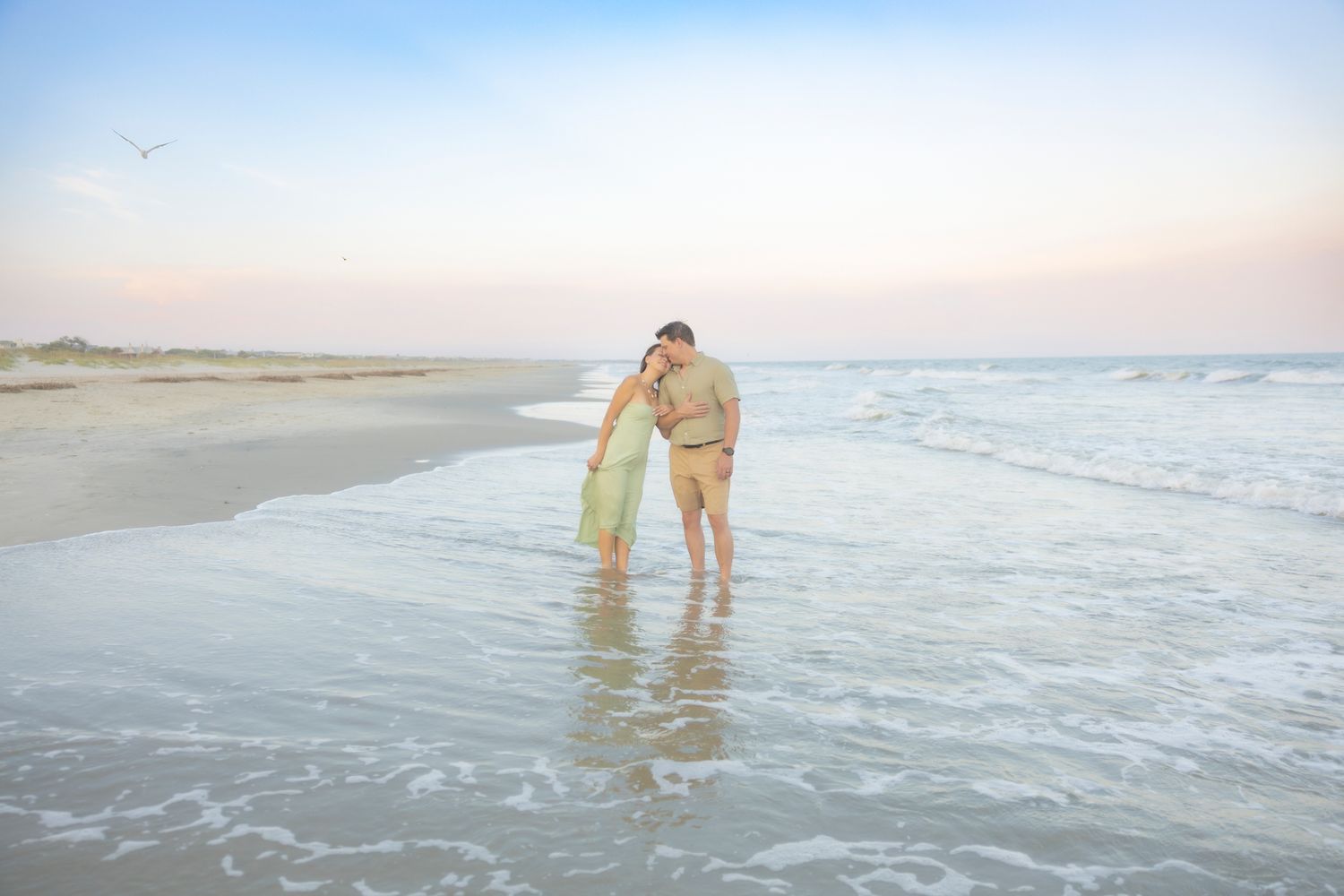 Couple embracing and kissing while standing in shallow beach waves during a soft pastel sunset on Isle of Palms.