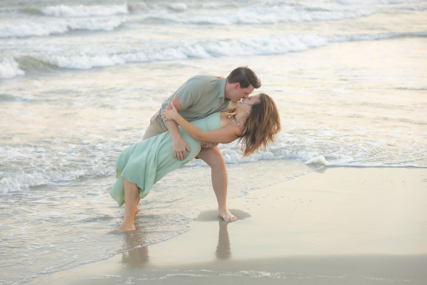 Romantic couple sharing a dip kiss in the ocean waves on a beautiful sandy beach.