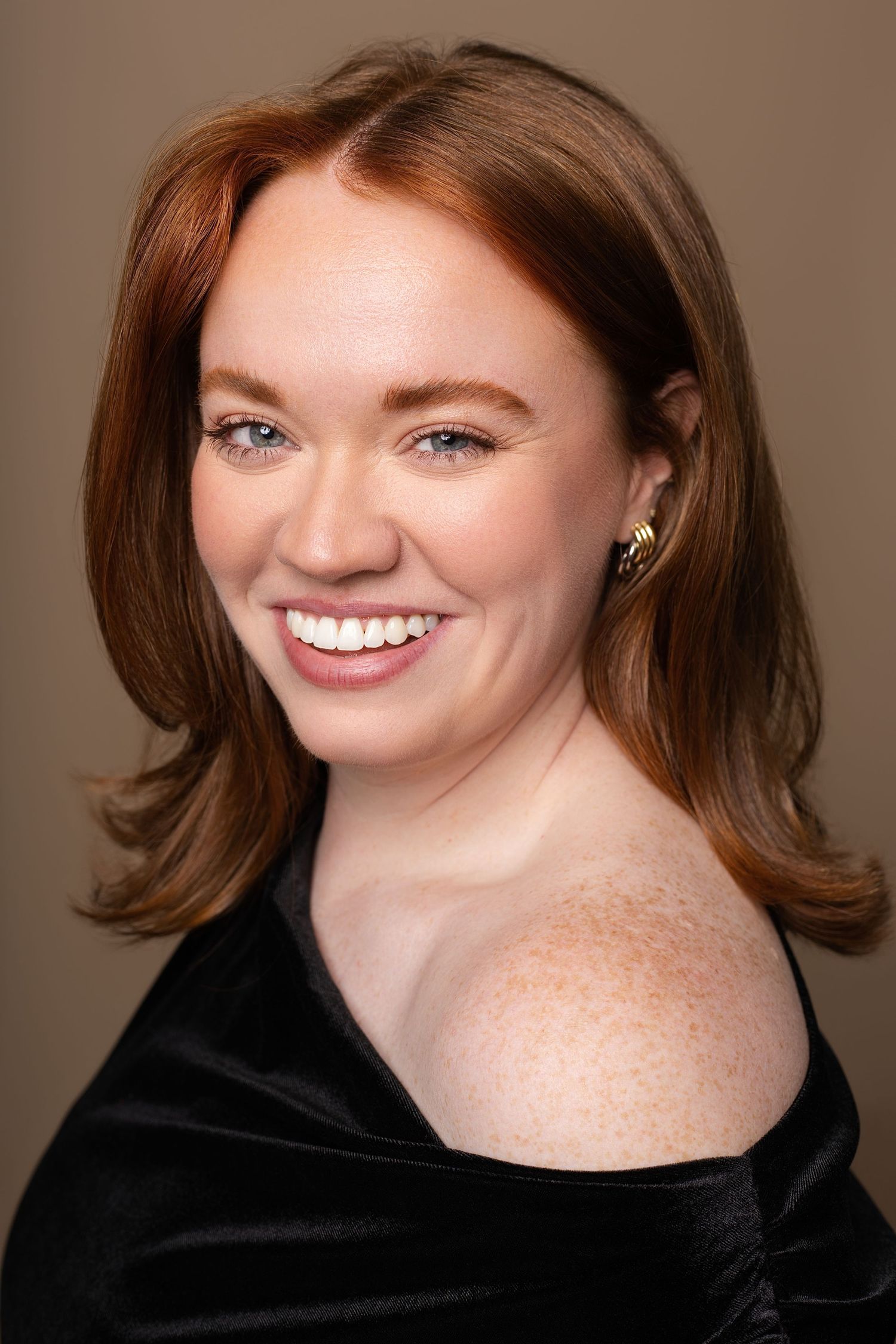 Smiling redhead woman with freckles in a black off-shoulder top for a headshot.